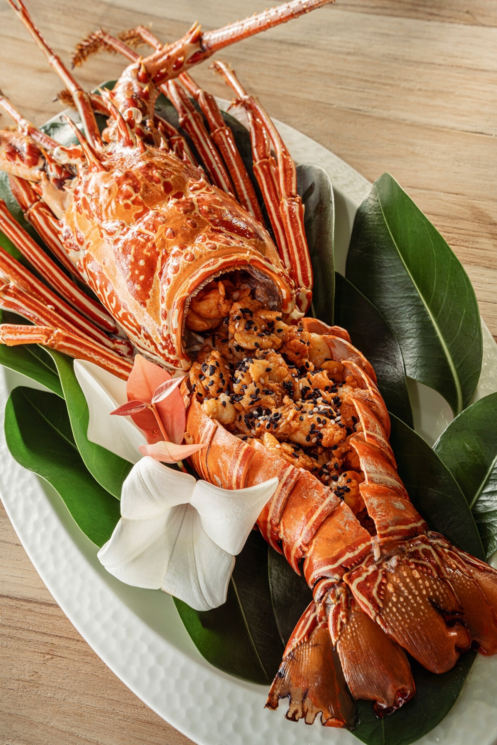 A whole cooked lobster with the shell cracked opened on a plate and seasoned with sesame seeds.