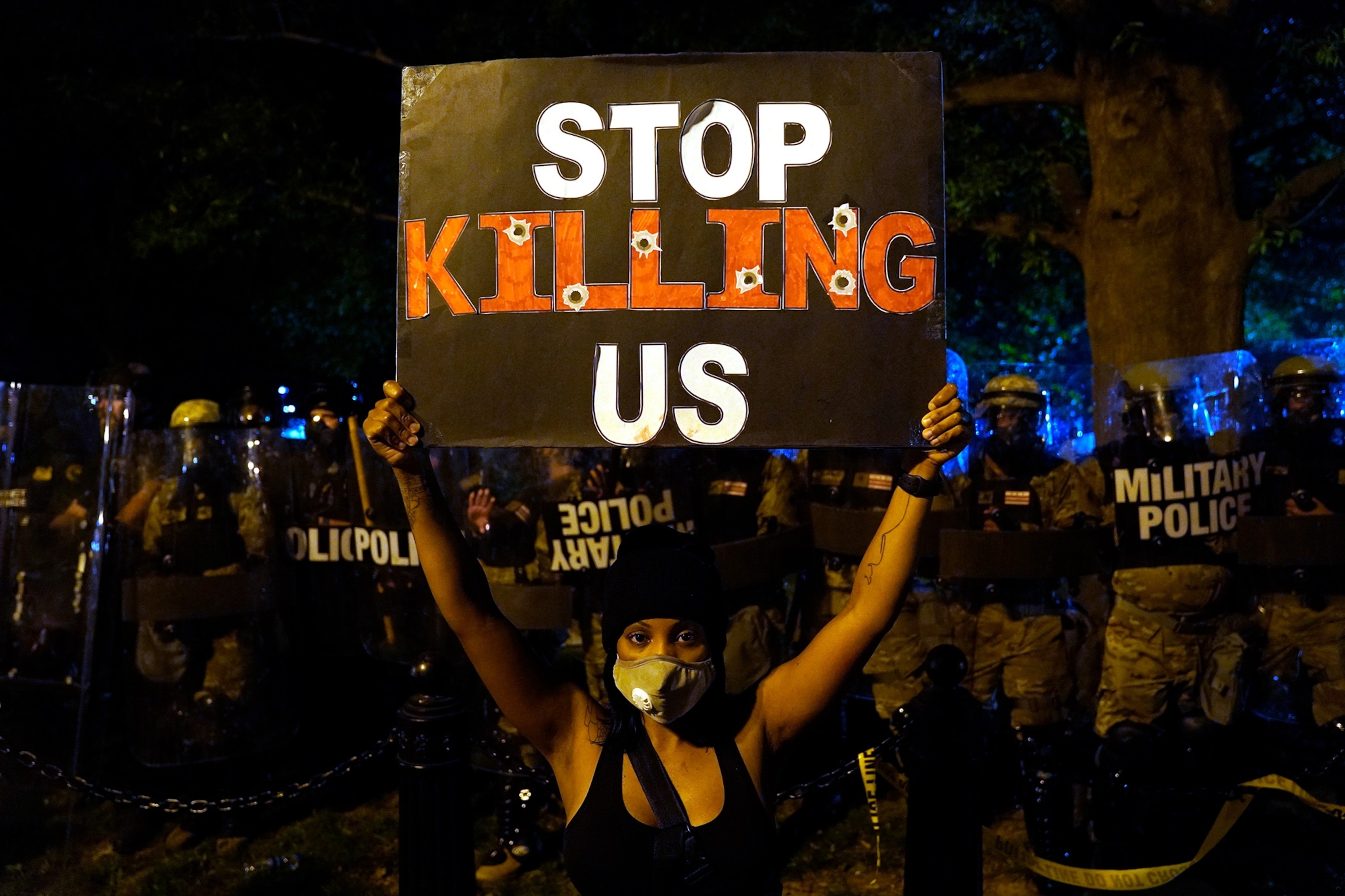 a protestor in front of a line of cops holding a sign that says stop killing us