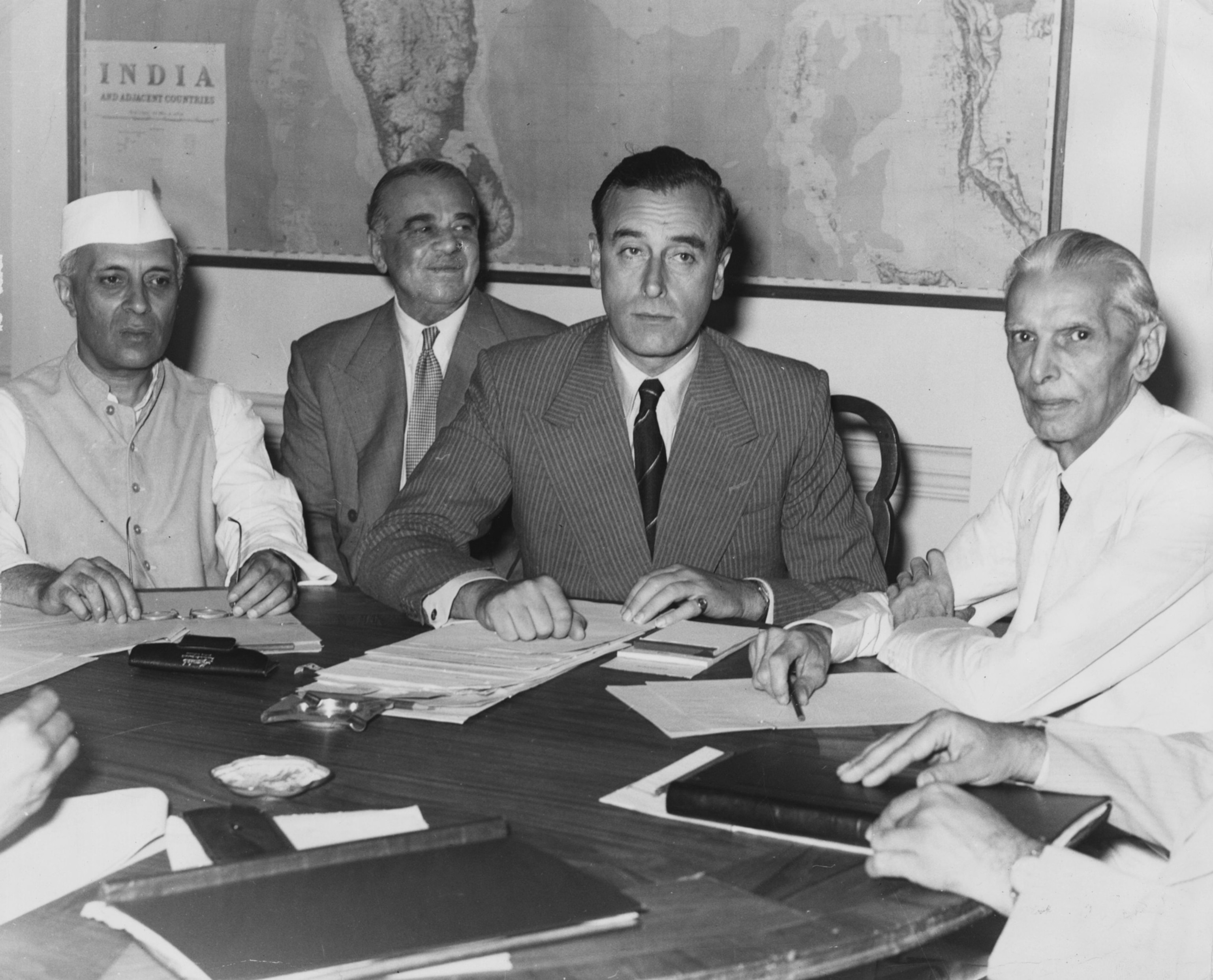 black and white photo of men at table with India map in background