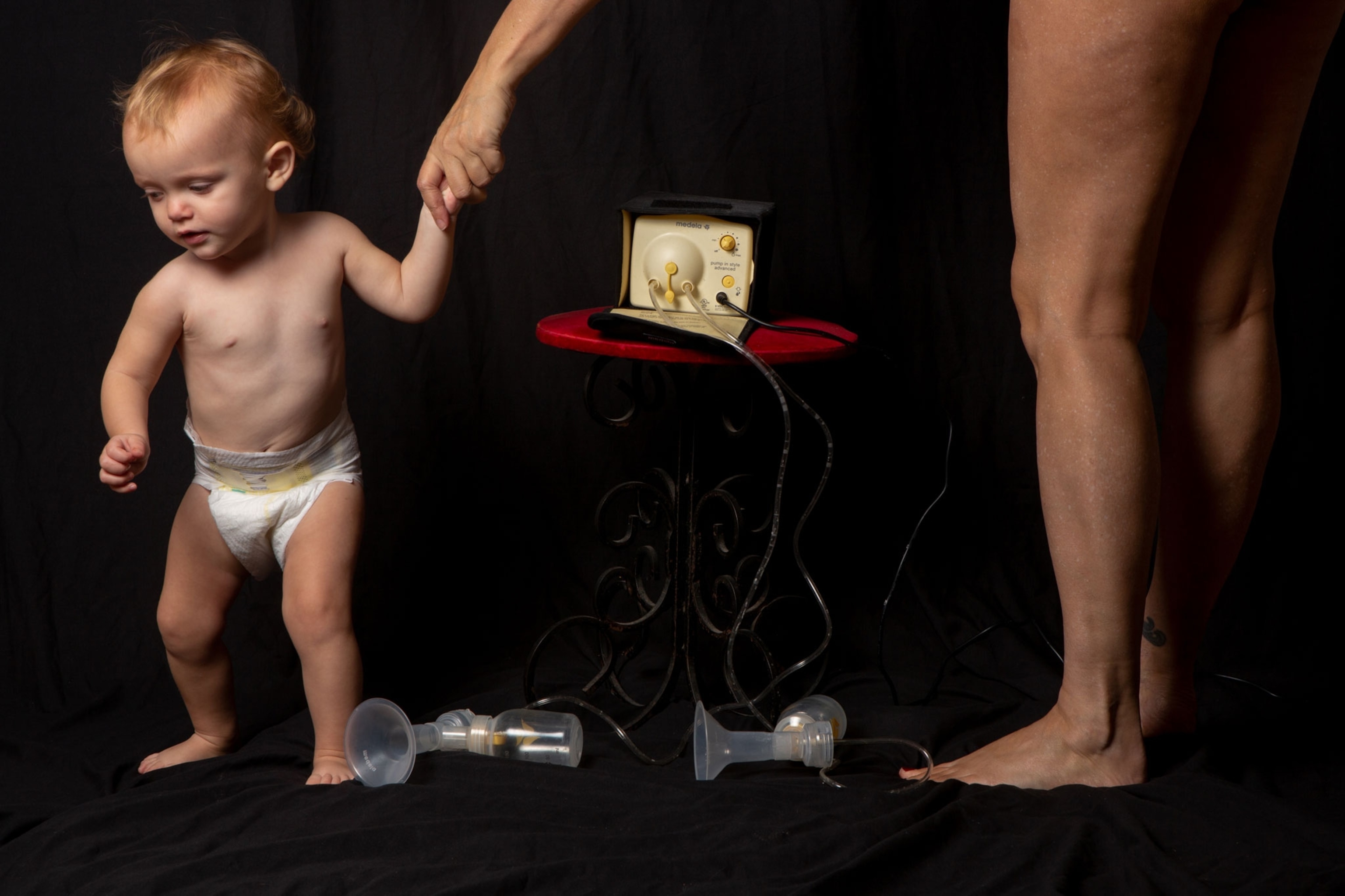 The mother holds her young daughter's hand next to a breast pump in a studio scene.