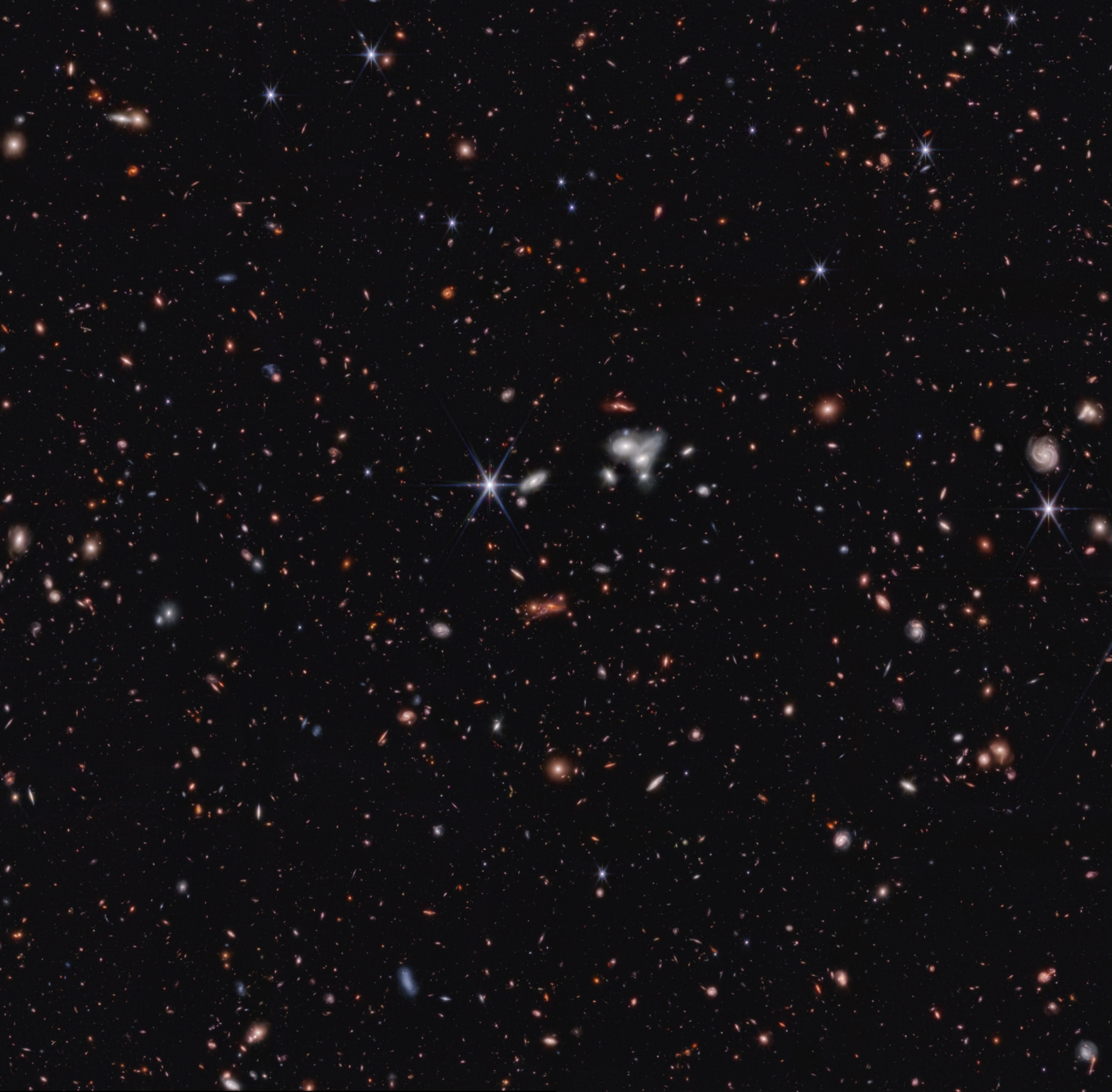 An expanse of thousands of galaxies of various colors, some appearing as swirls and others as balls of light.