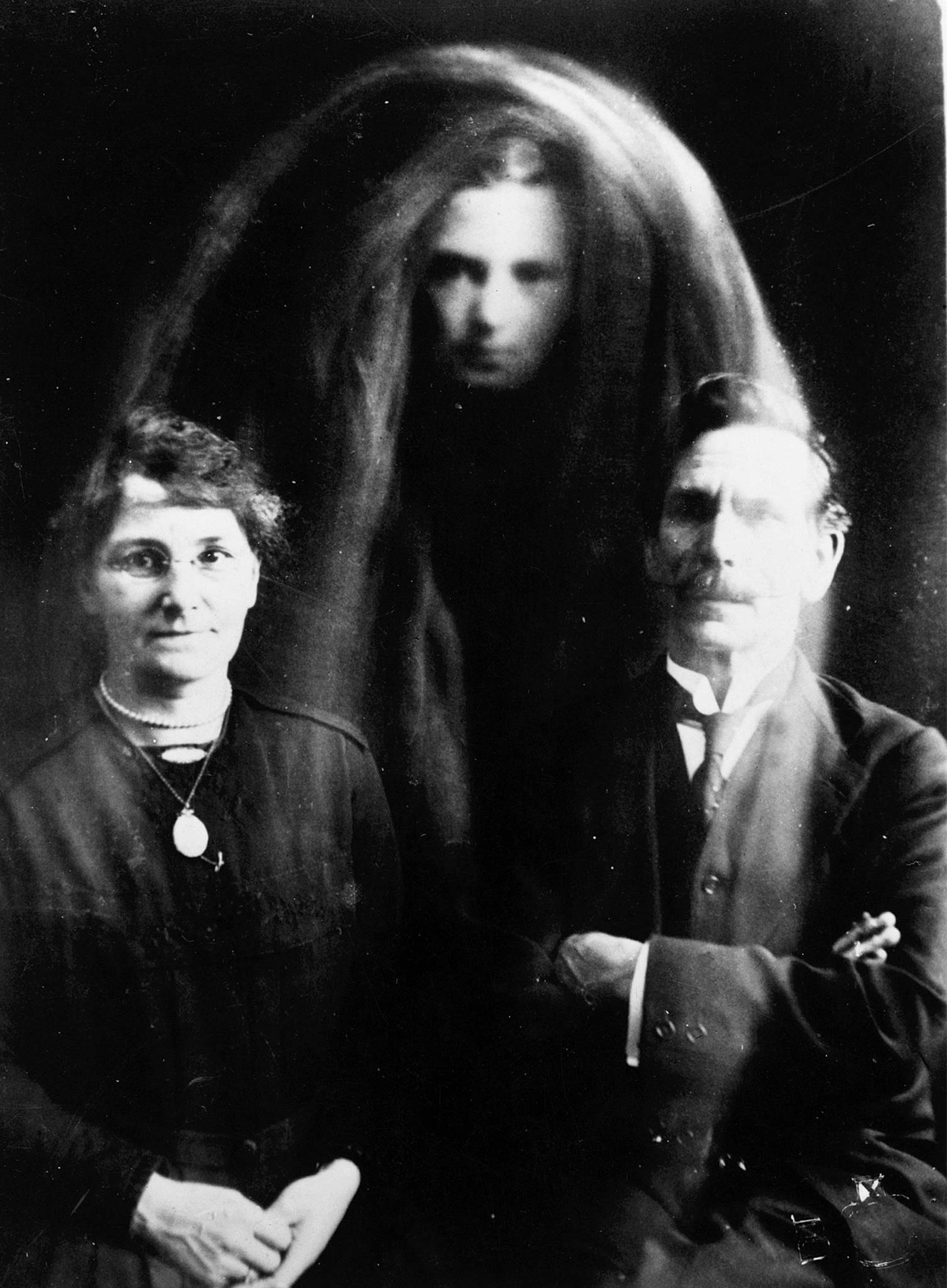 A supposed spirit photograph from circa 1900 with a ghost behind two people seated for a portrait