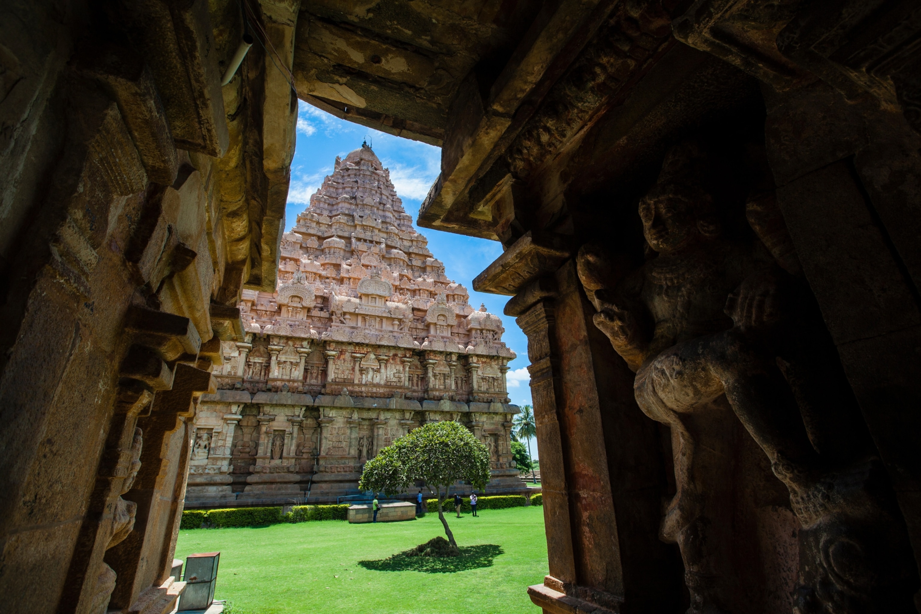 A wall of carved figures leads to an opening that reveals a temple in the distance