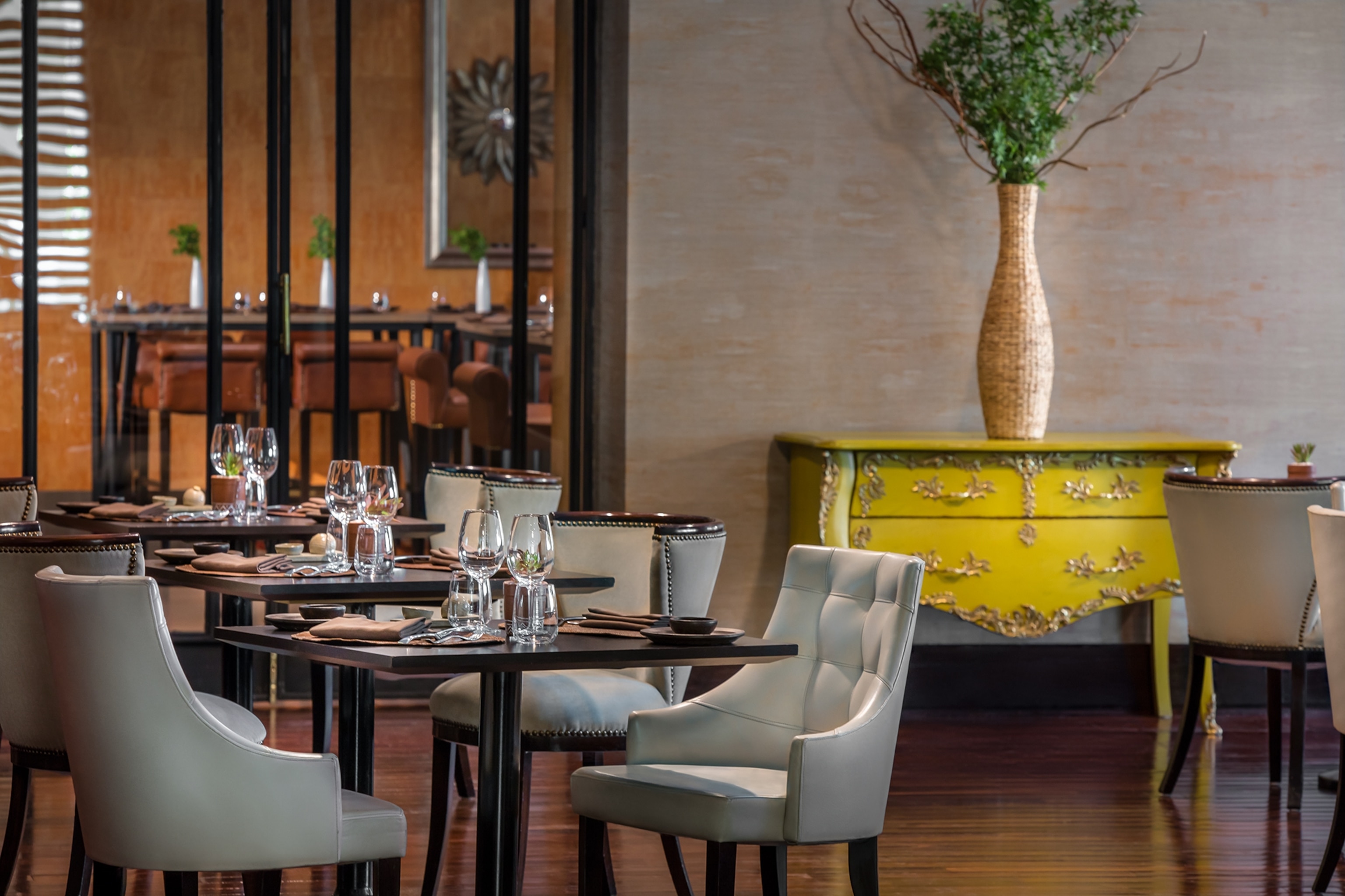 A picture of a swanky restaurant in Santiago. The chairs are grey and tables are wooden, in the background a yellow chest decorates the room.