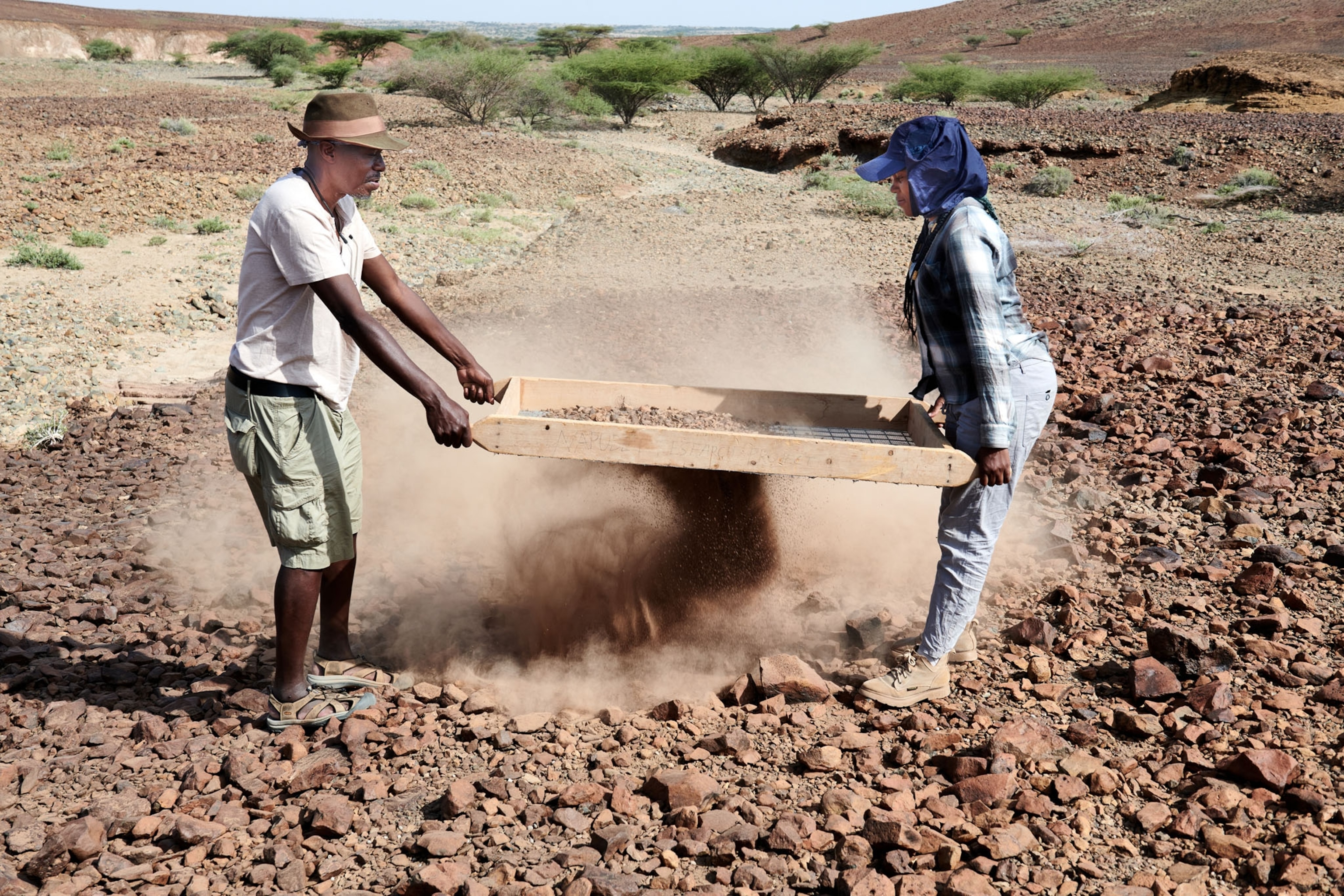 Picture of two people sifting dirt outside