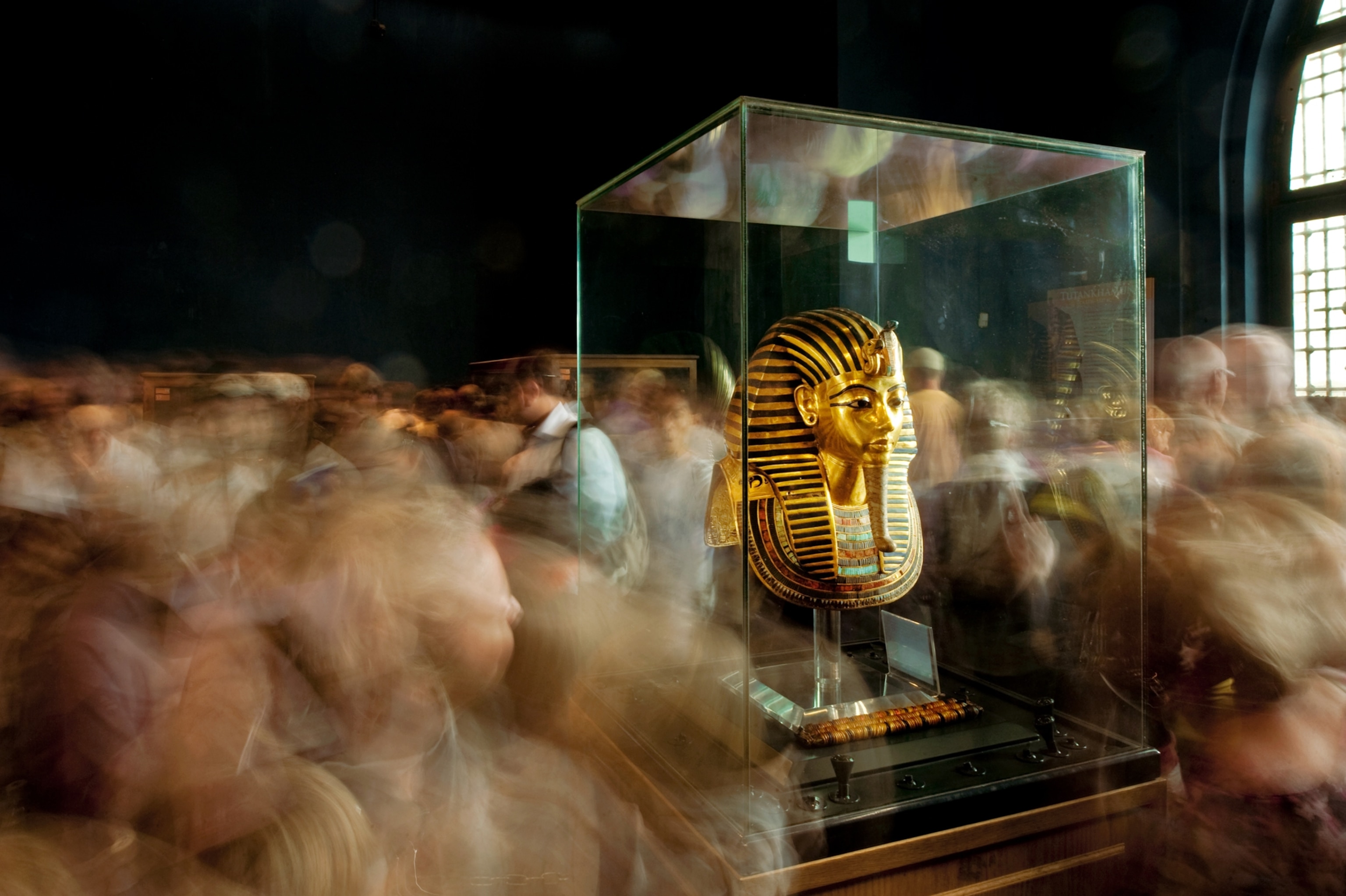 Picture of golden mask in glass display surrounded by crowd.
