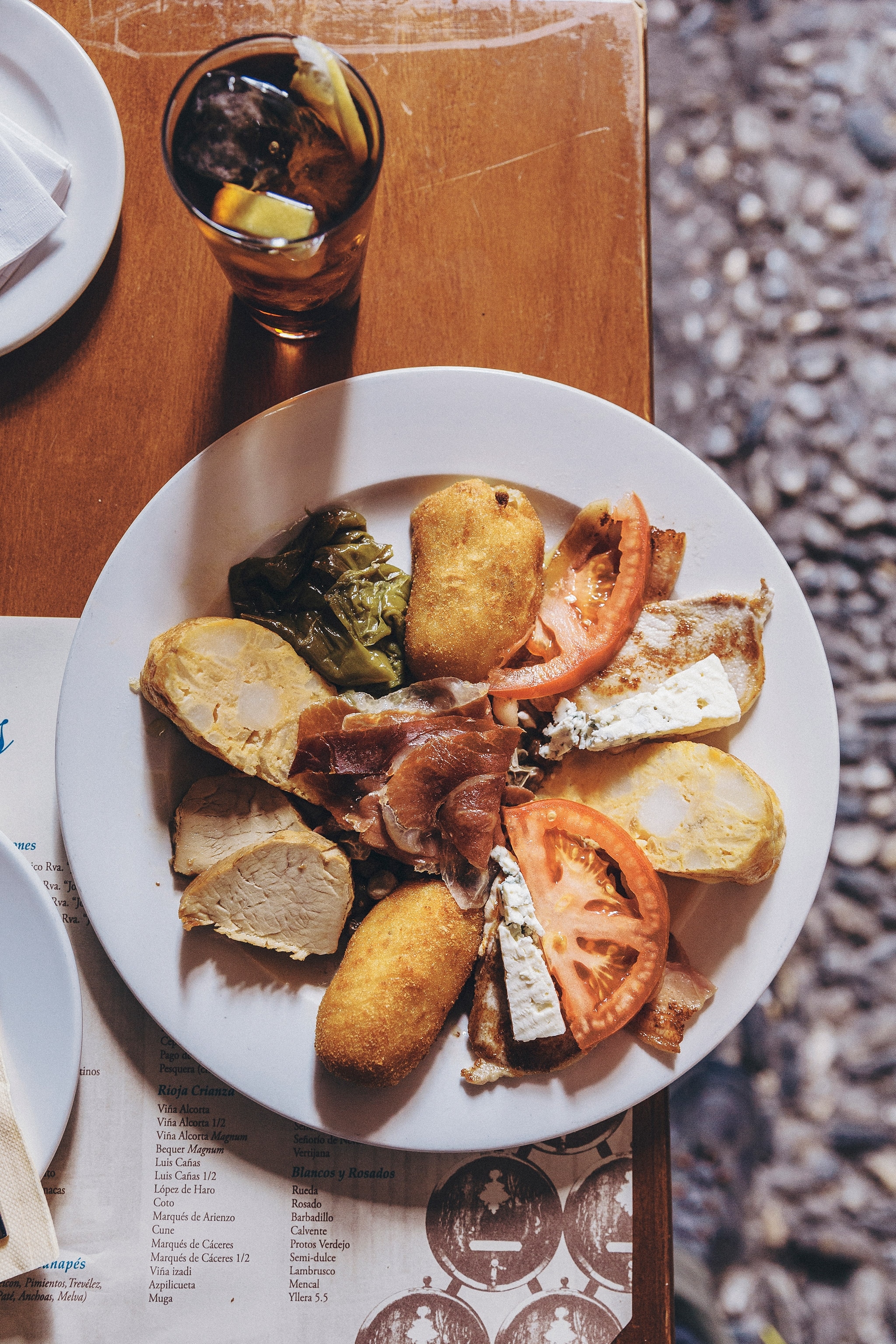 A glass of vermouth and a sharing plate of tapas on a table on the terraza of Bodega Castañeda