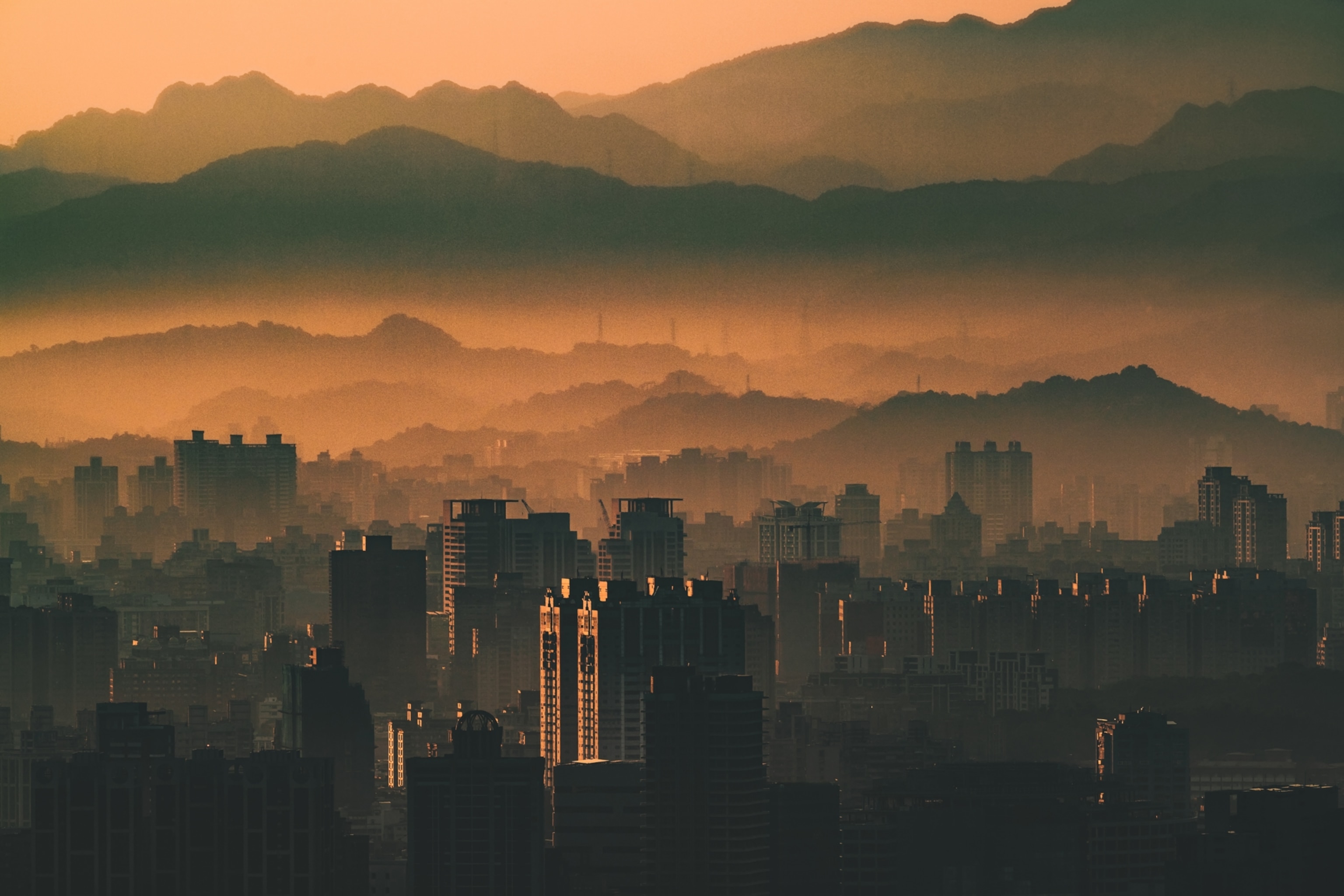 An elevated view of Taipei's skyline at sunrise. Layers of mountains disappear into layers of fog and smog in the background.