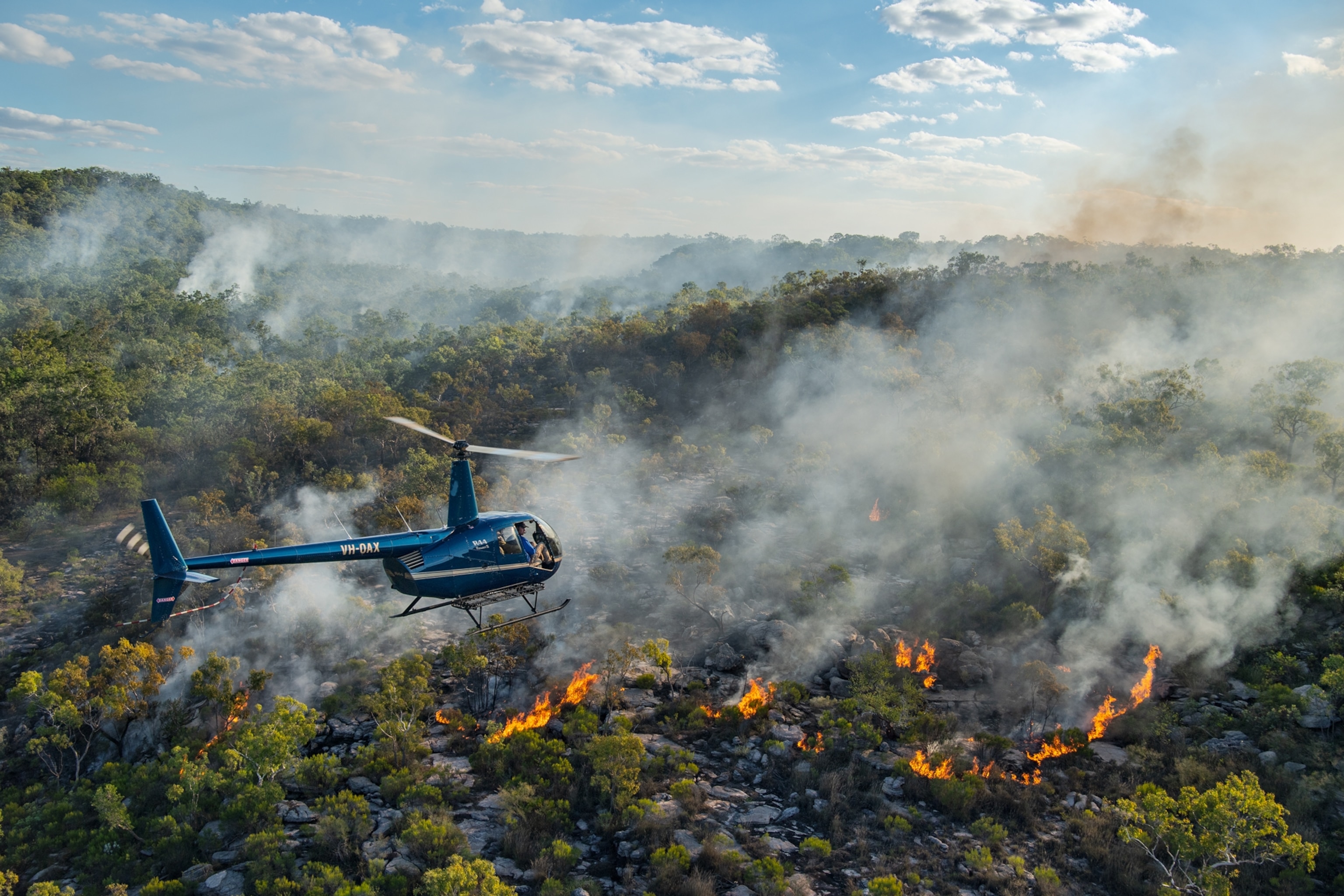Picture of helicopter over forest with smoke over it.