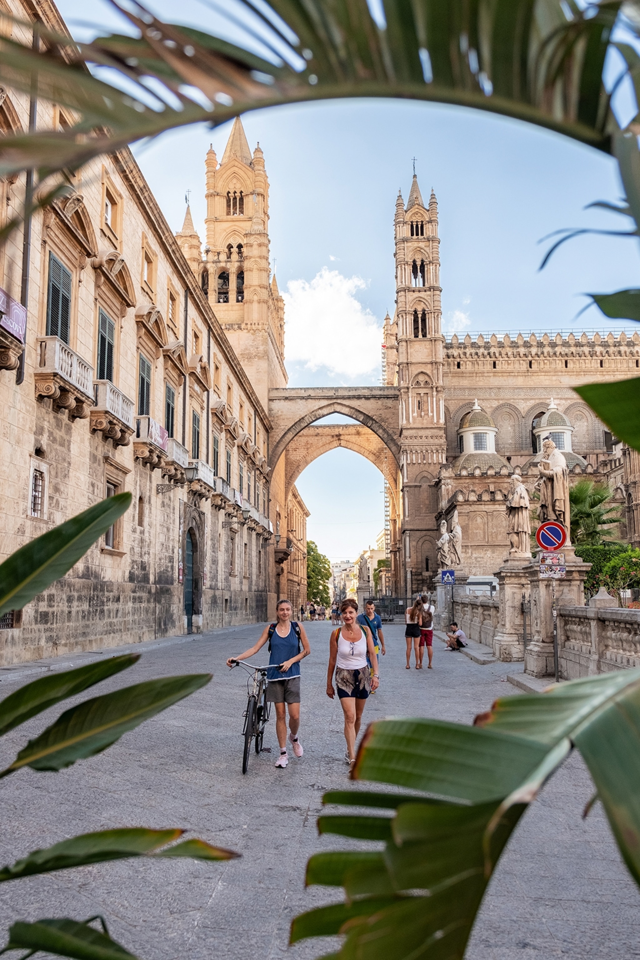 Two women walking pushing a bike down the street surrounded by grand architecture