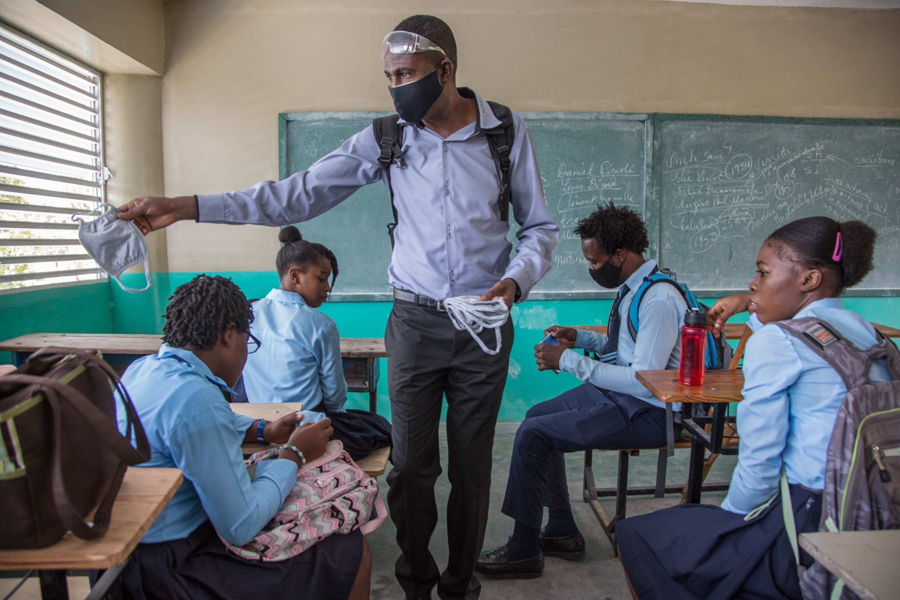 a worker hands out masks to children in a school in Haiti
