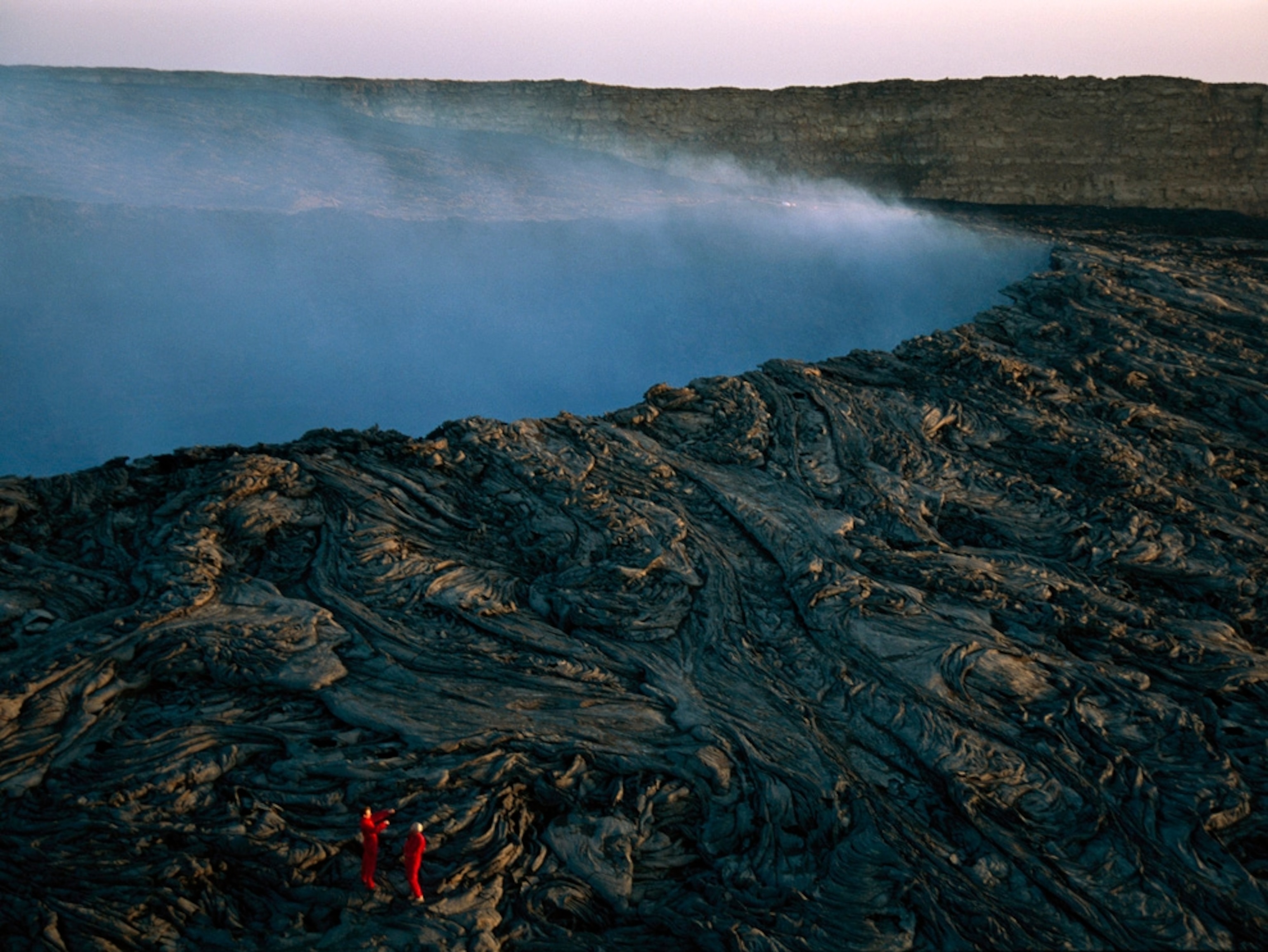 Climbers walk on lava at a steaming volcano crater