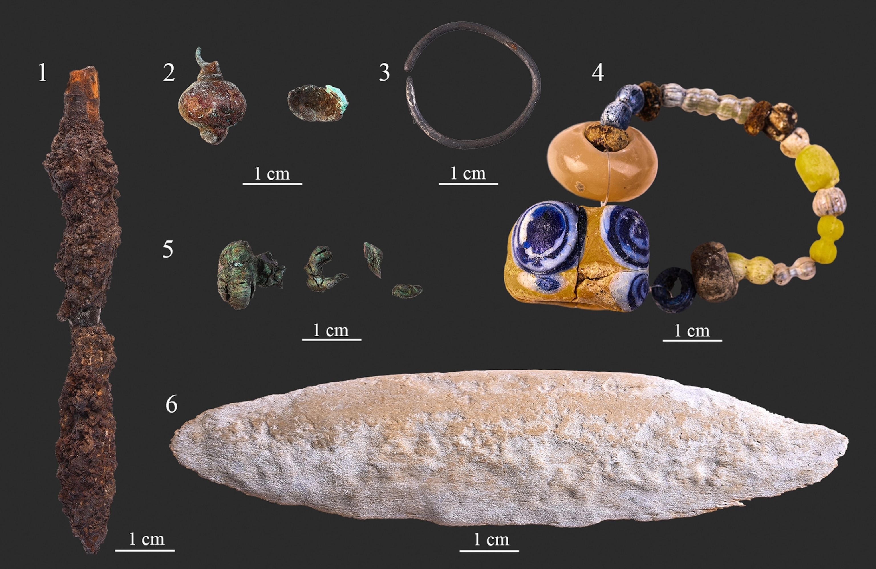 Artifacts found in grave No. 63 including a long stone arrowhead; a button; a silver ring; a string of yellow, white, and blue beads; and an antler bow plate.