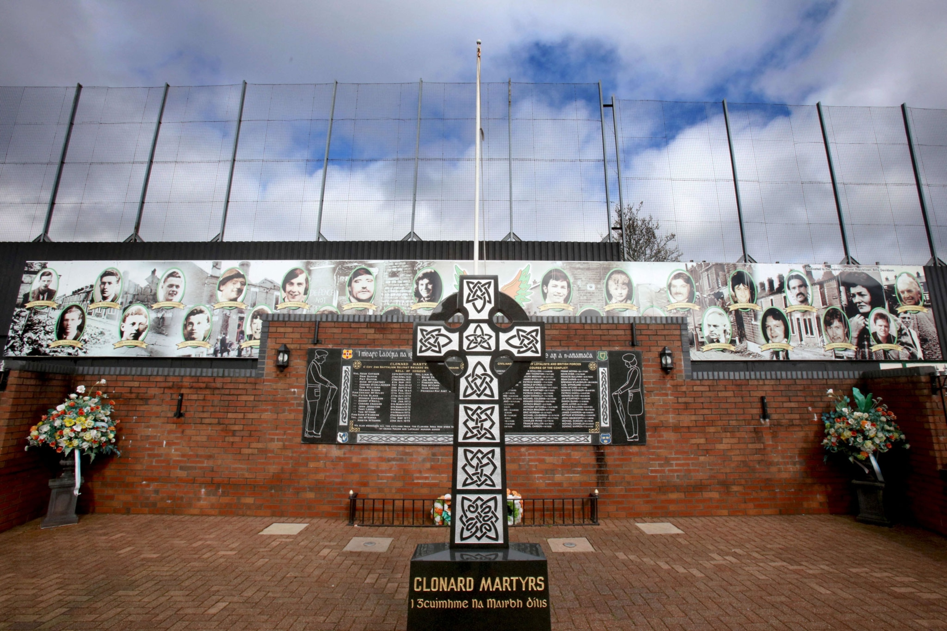 a memorial for IRA volunteers in front of a peace wall in Belfast, showing a cross and photos of people displayed behind it