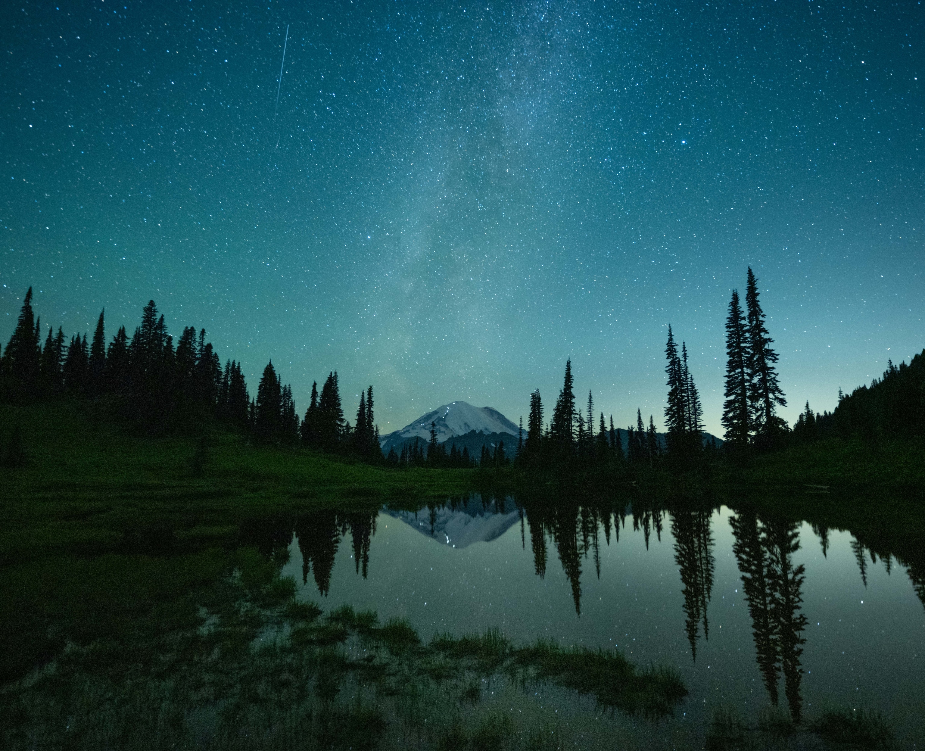 A line of headlights dot Mount Rainer at night, with the stars above and Tipsoo Lake in the foreground