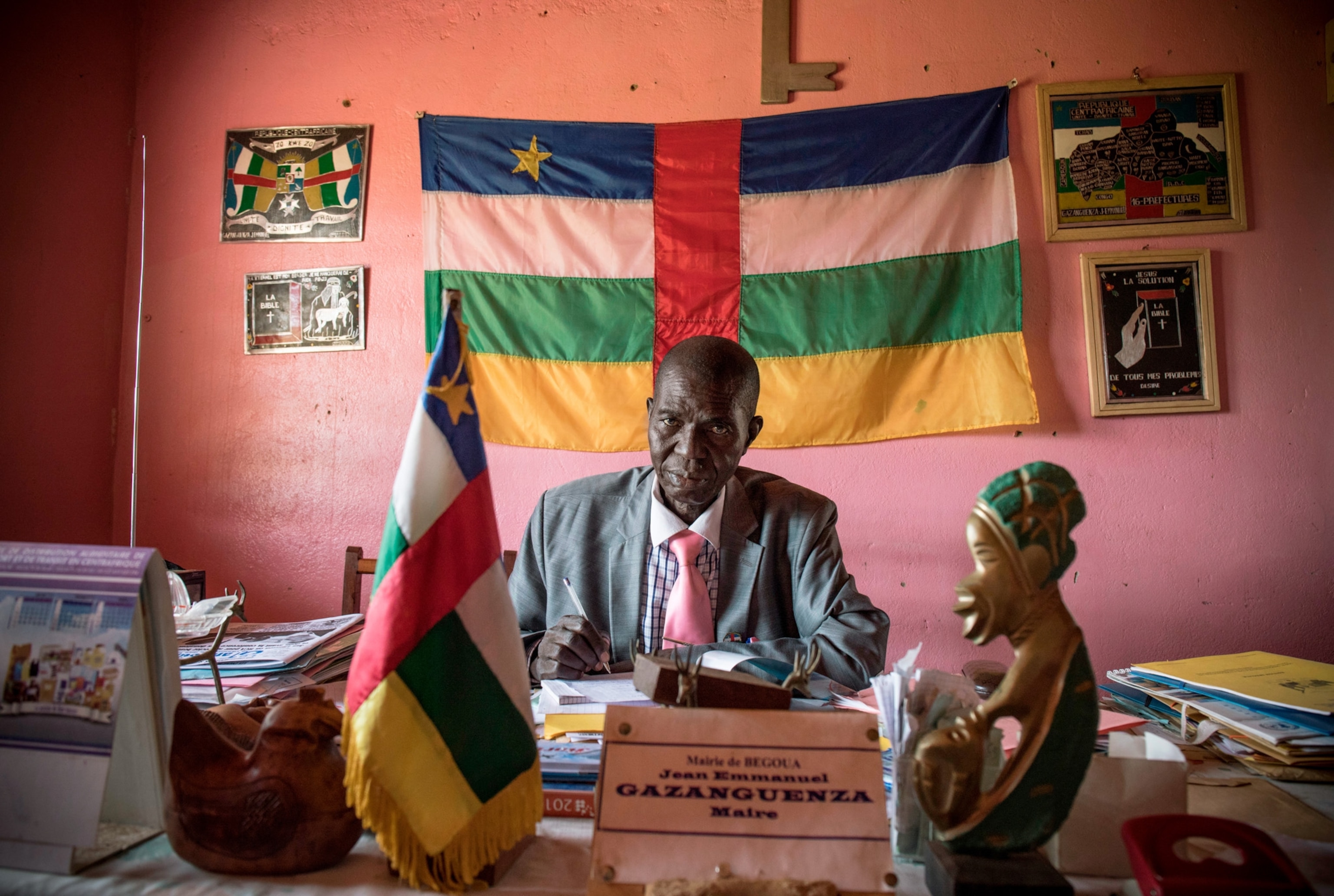 the mayor in Bangui sitting at his desk with the flag of his country behind him