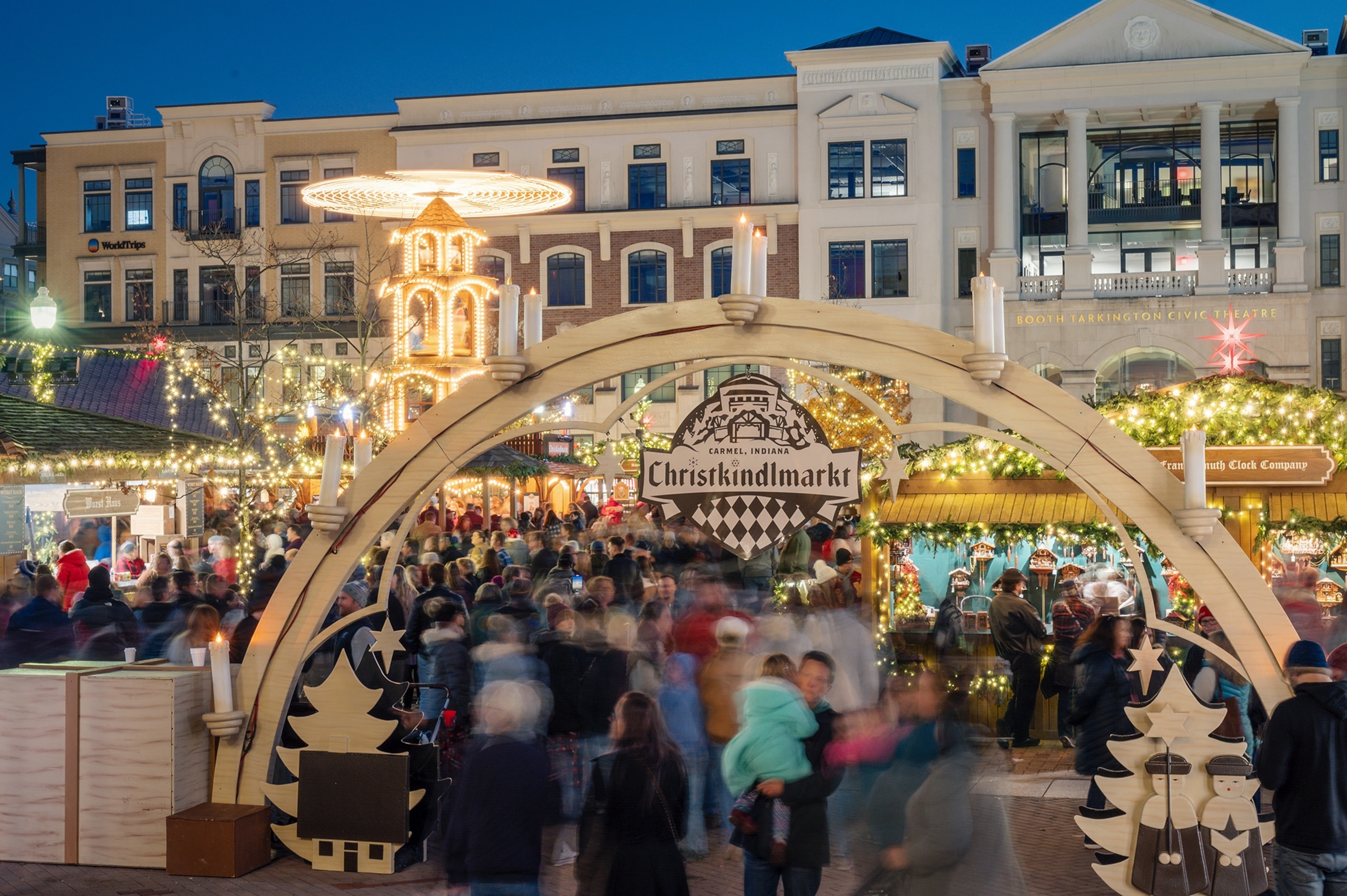 Holiday lights and blurred people at the entrance to the Carmel Christkindlmarkt at night.
