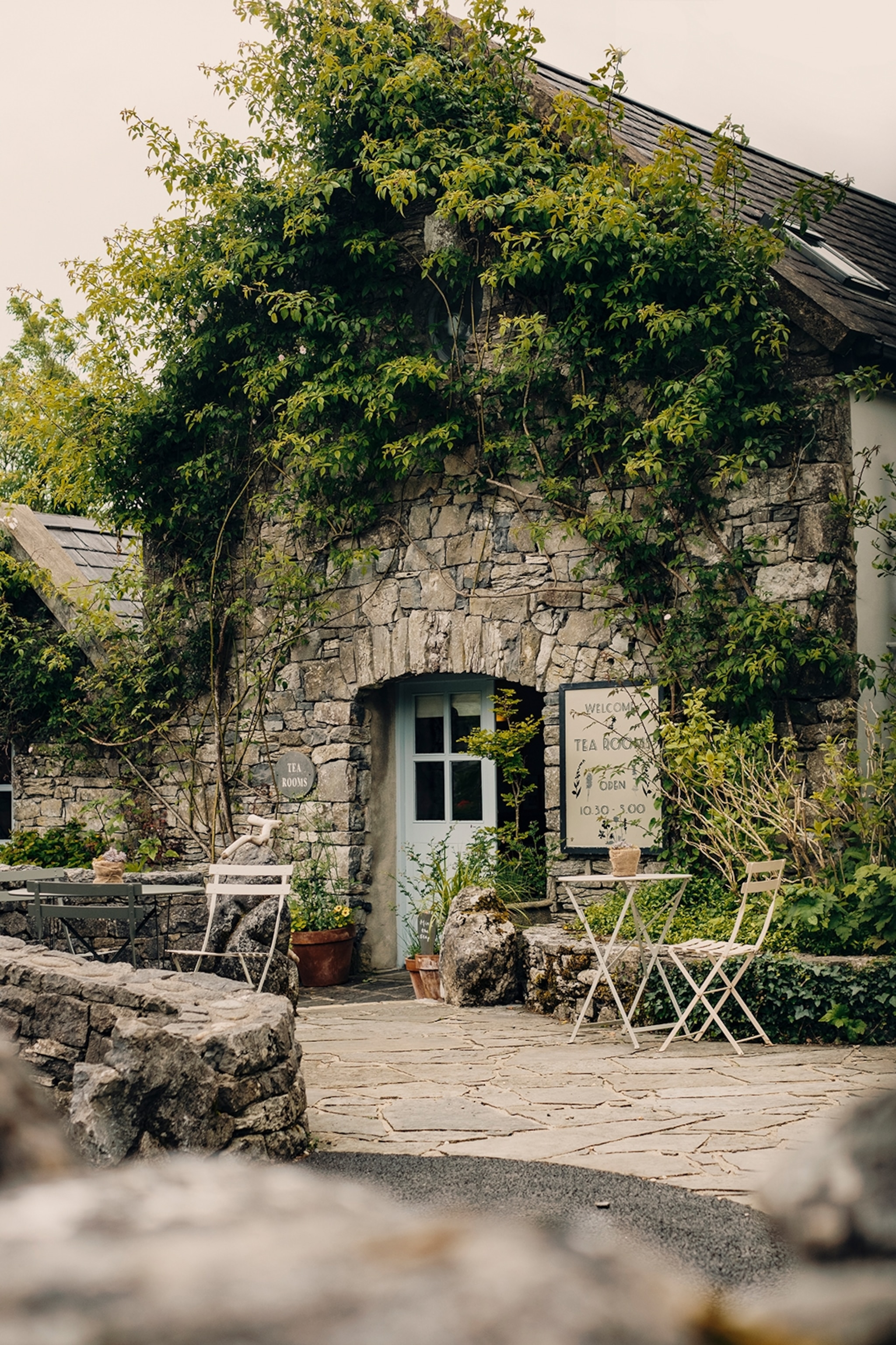 Stone cottage with tables and chairs outside and vines covering the exterior of the cottage