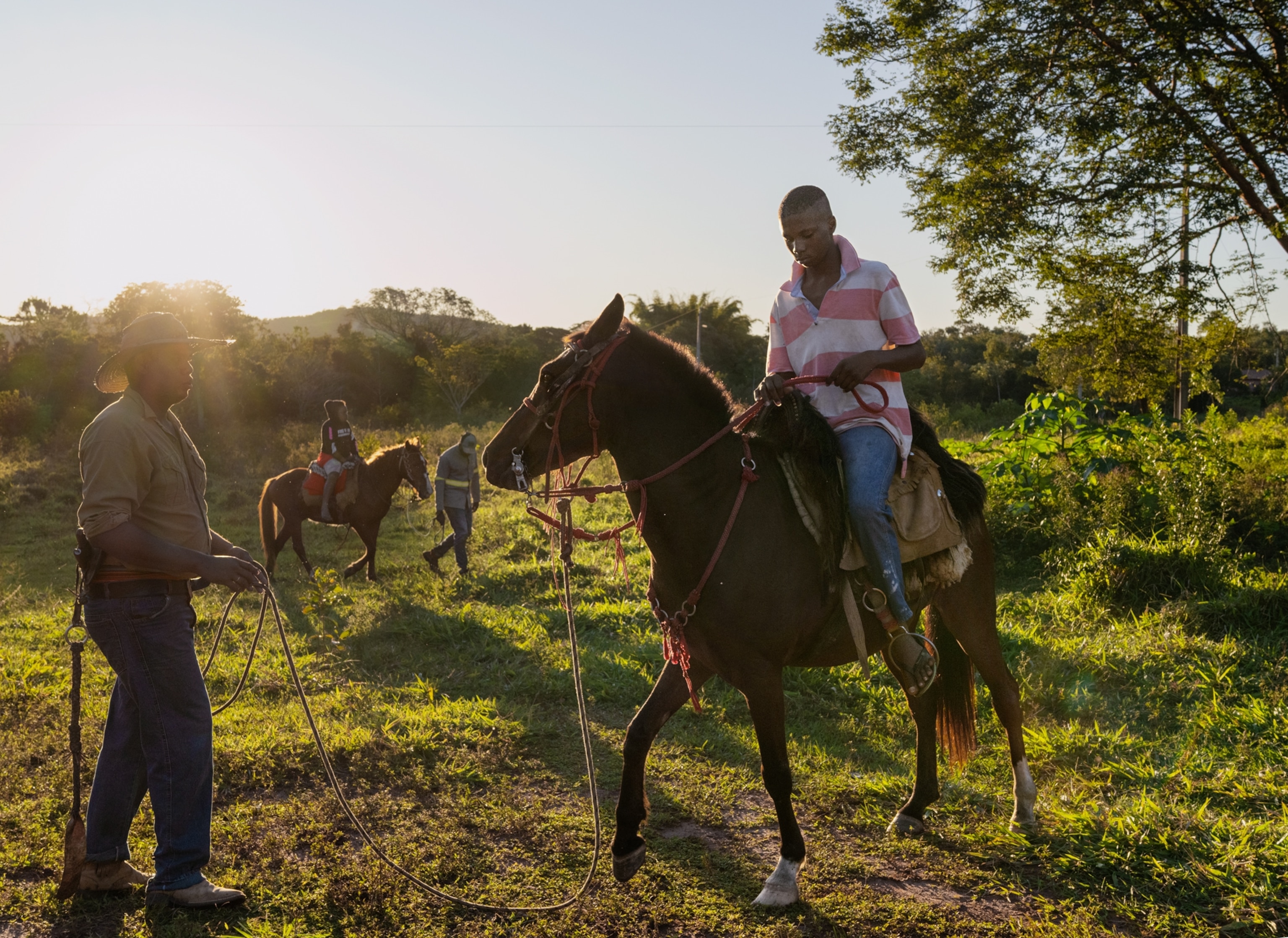Two people are riding horses each with someone standing in front of them holding a rope.