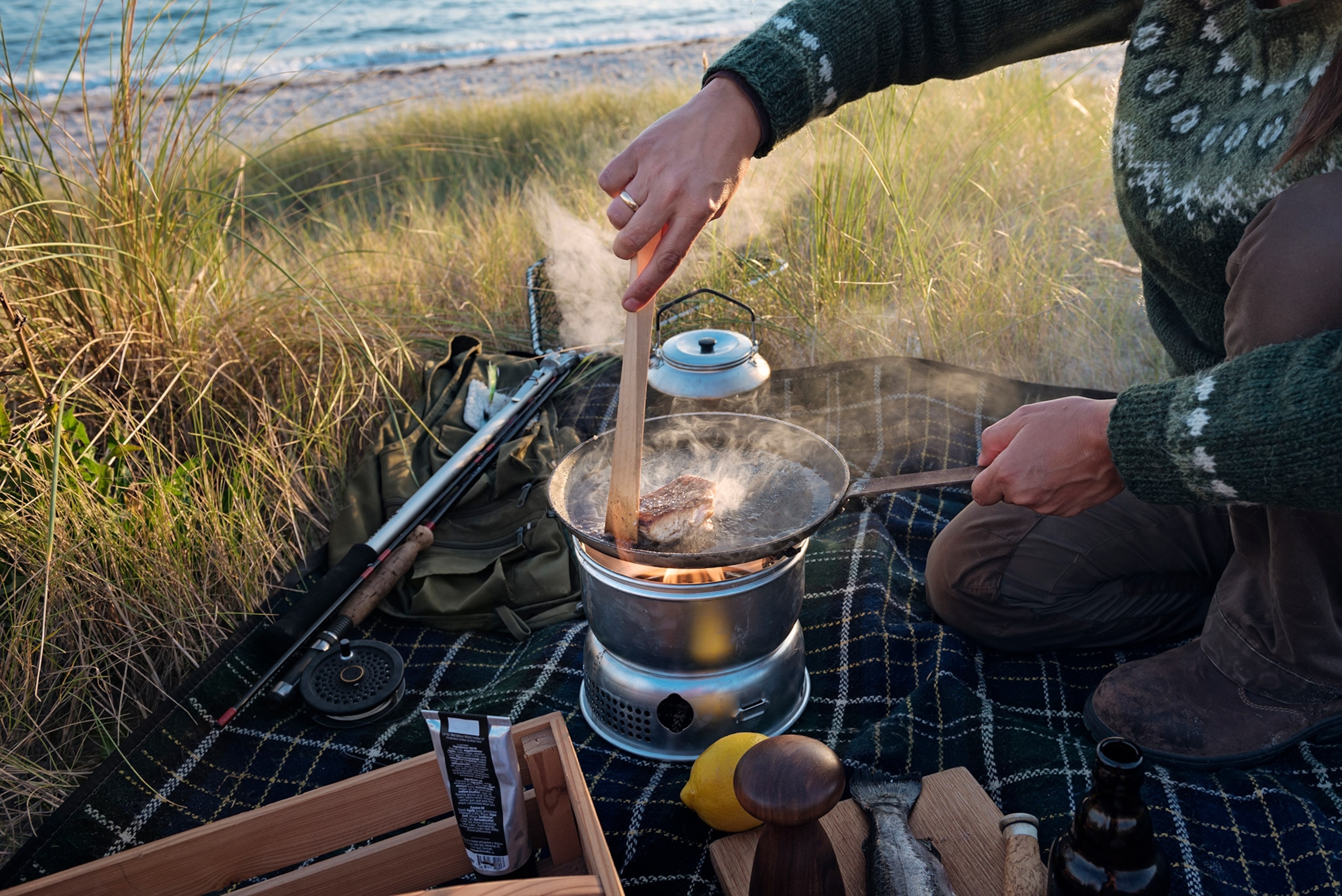 Fisherman cooking her catch at the beach. She is using a gas camping stove in a sheltered spot in the dunes next to the beach where she was fishing.