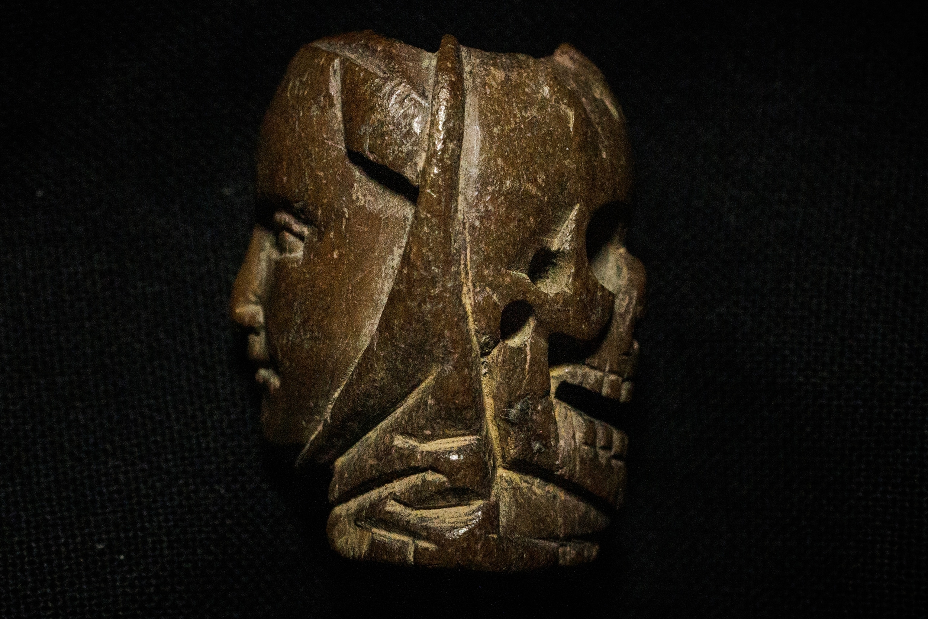 A carved bone rosary bead featuring a face on one side and a skull on the other.