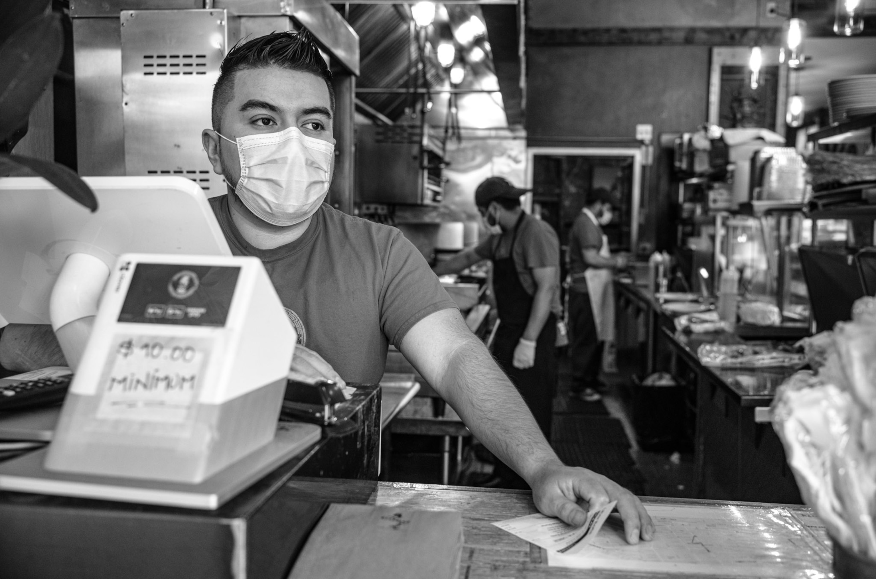a cashier at a restaurant with the cooks in the background
