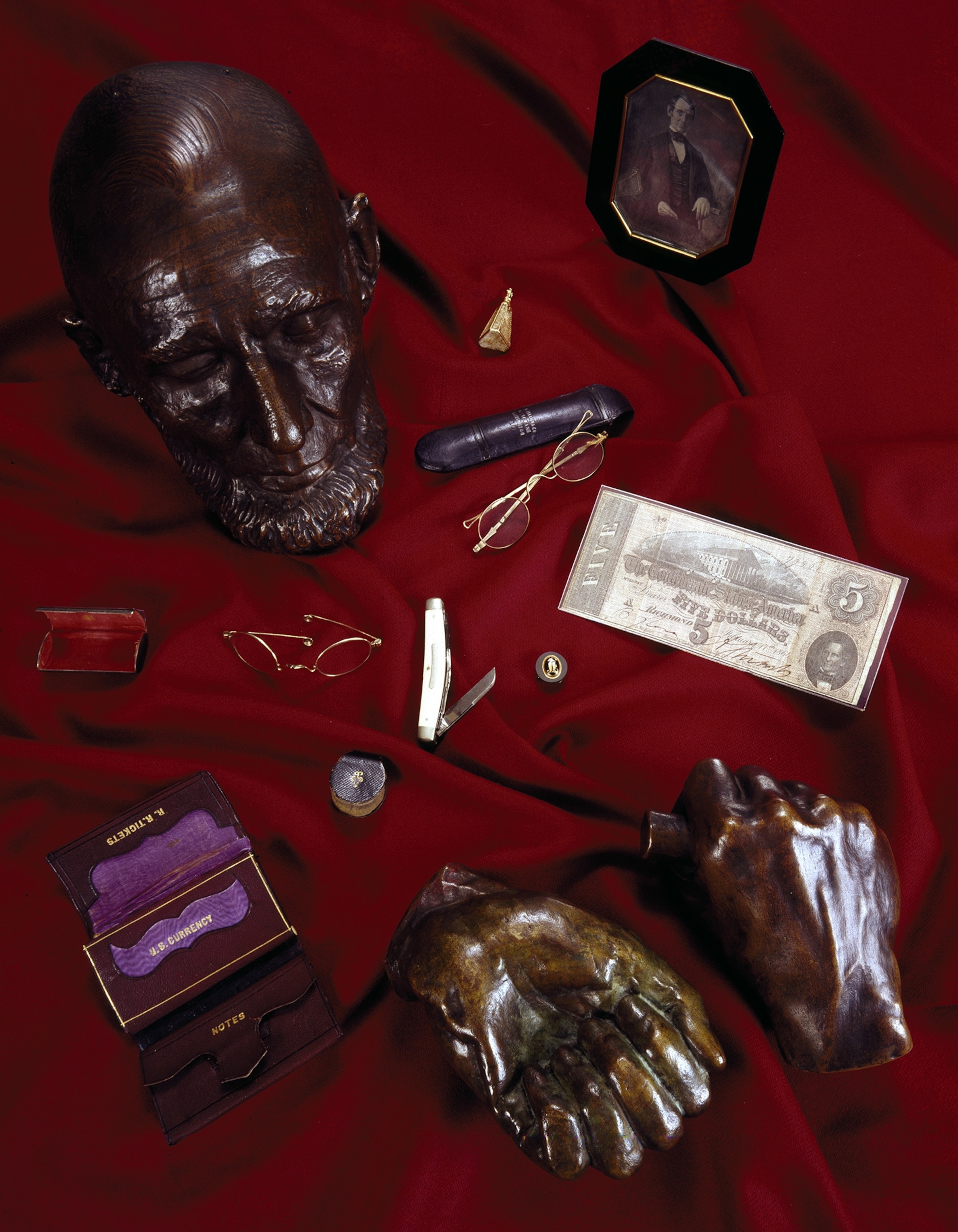 Bronze casting of the death mask of Abraham Lincoln and what was in his pockets the night he died in 1865 against a red cloth.