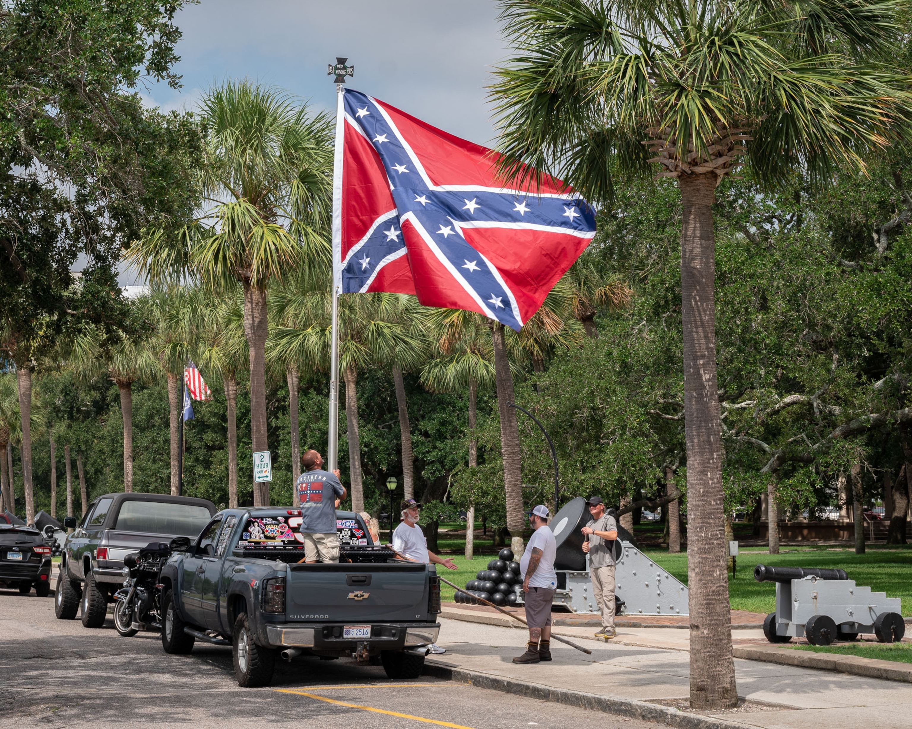A person in a pick-up truck flying confederateflag surrounded by a few people