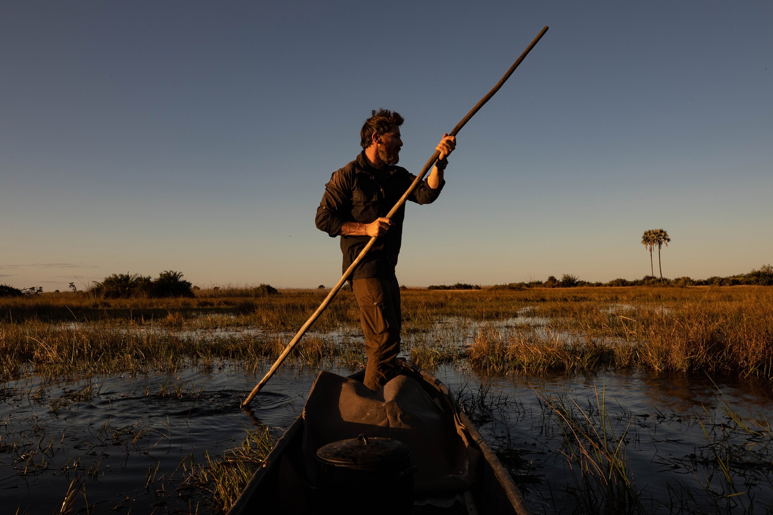 A man standing up, rowing a boat.