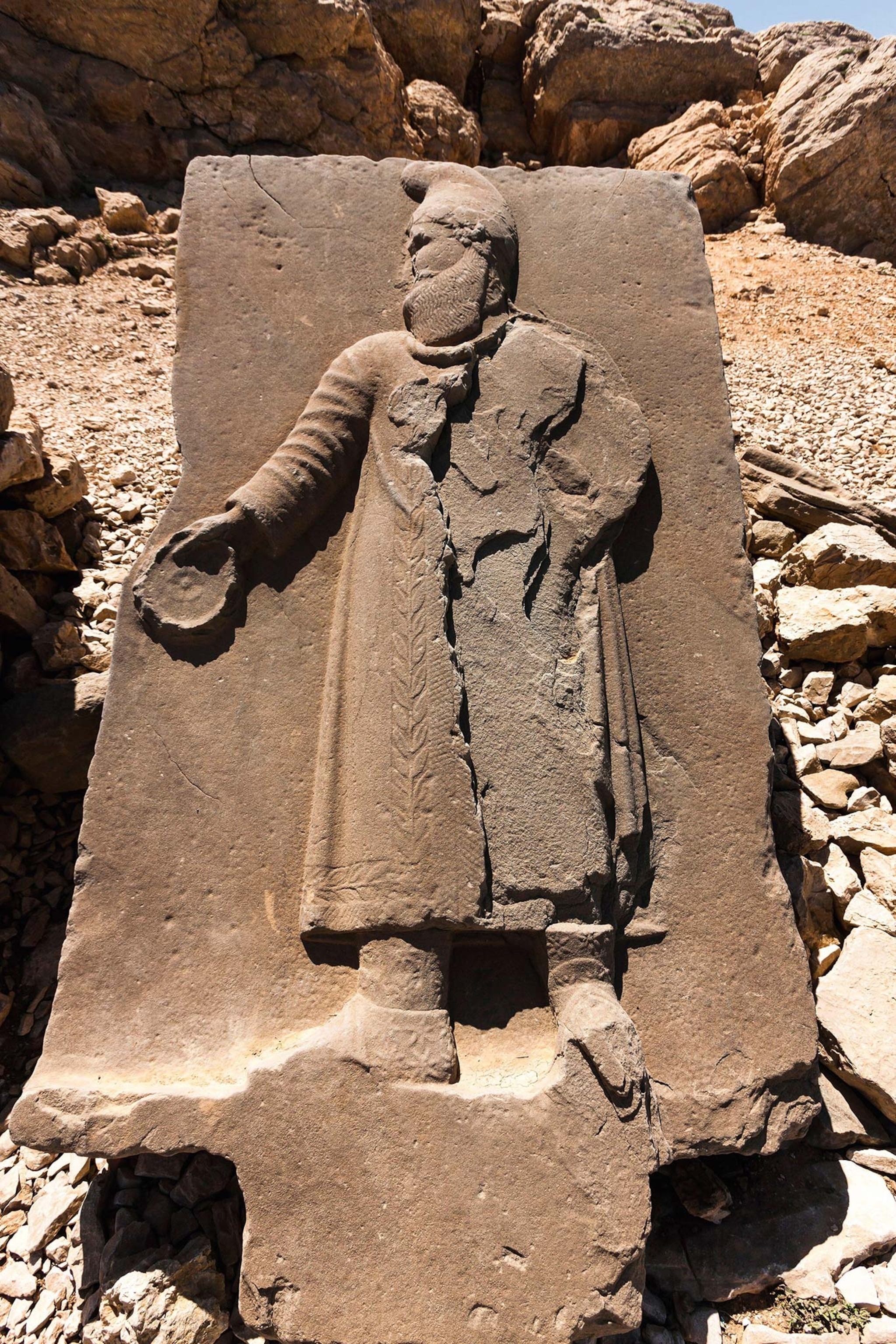 A stone relief of a man's side profile wearing a Persian gown and Phrygian cap