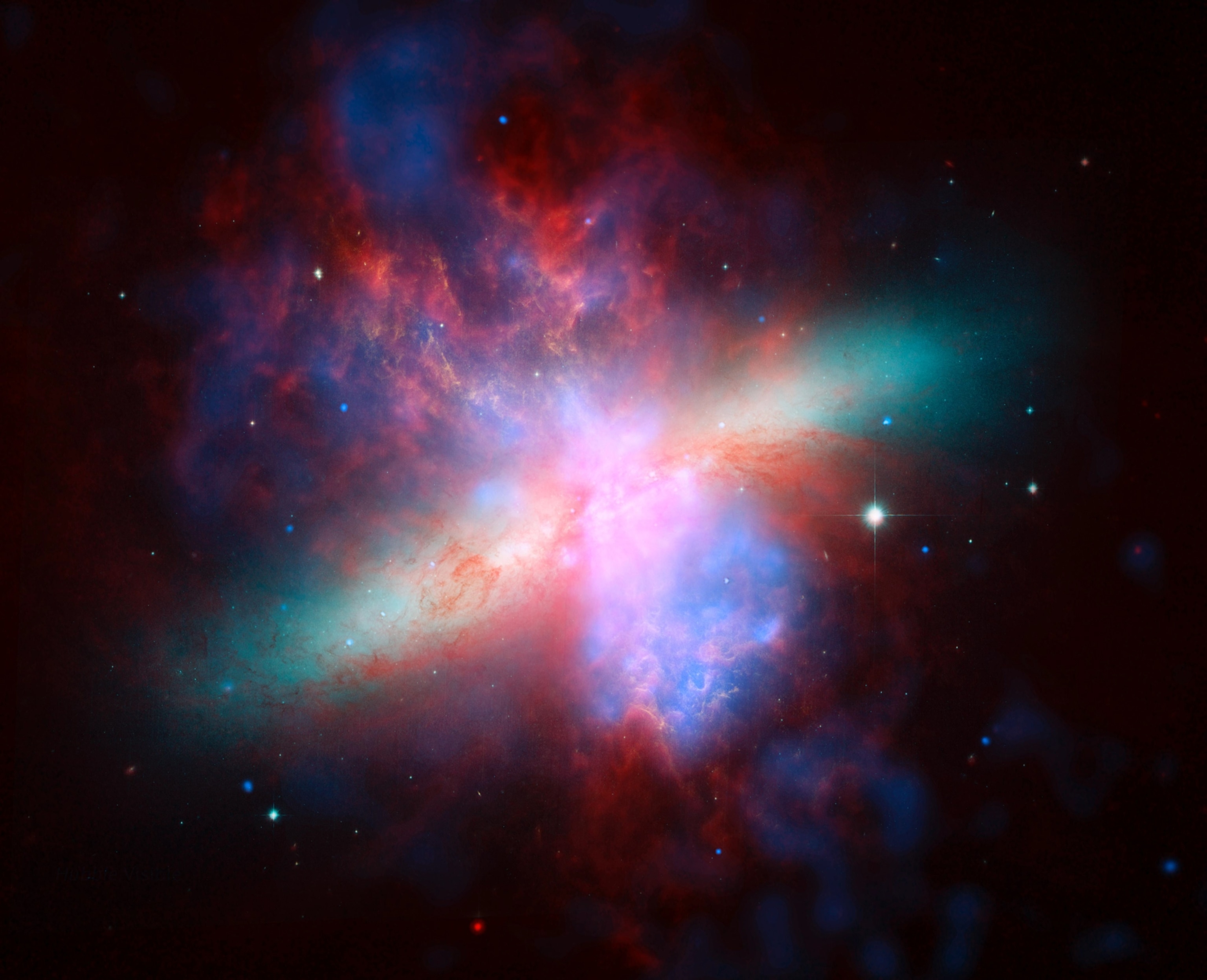 A false-colorized view of the M82 galaxy, revealing nebulous clouds in shades of red and orange interspersed with large gaseous discs of blue and turquoise.