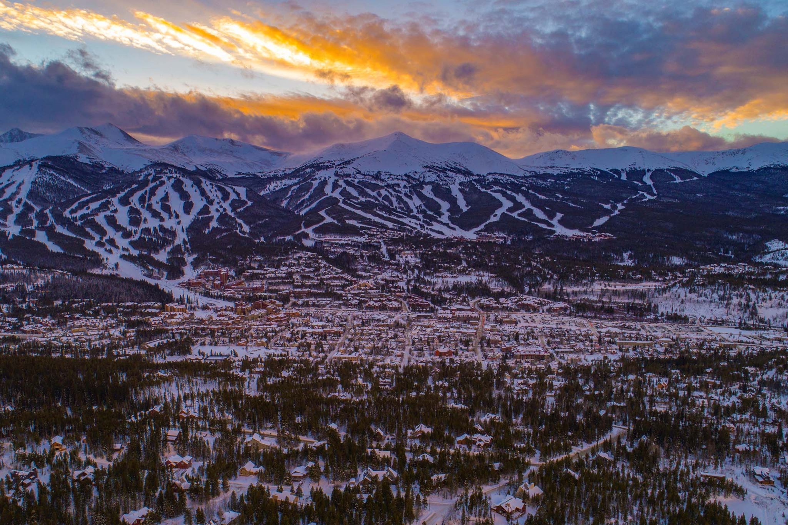Elevated view of a town surrounded by mountains and snow at sunset