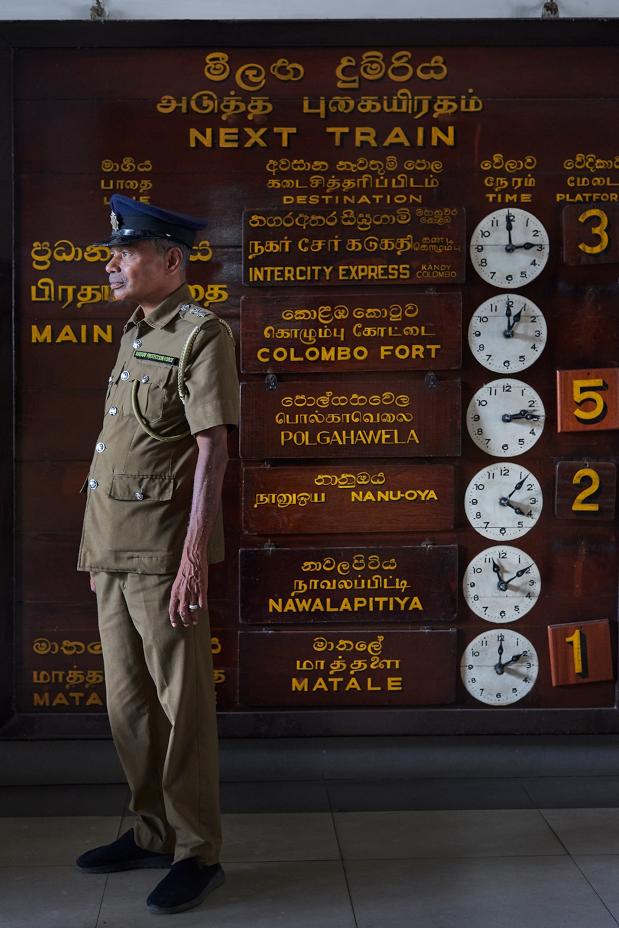 Train conductor standing next to a vintage looking train arrivals board
