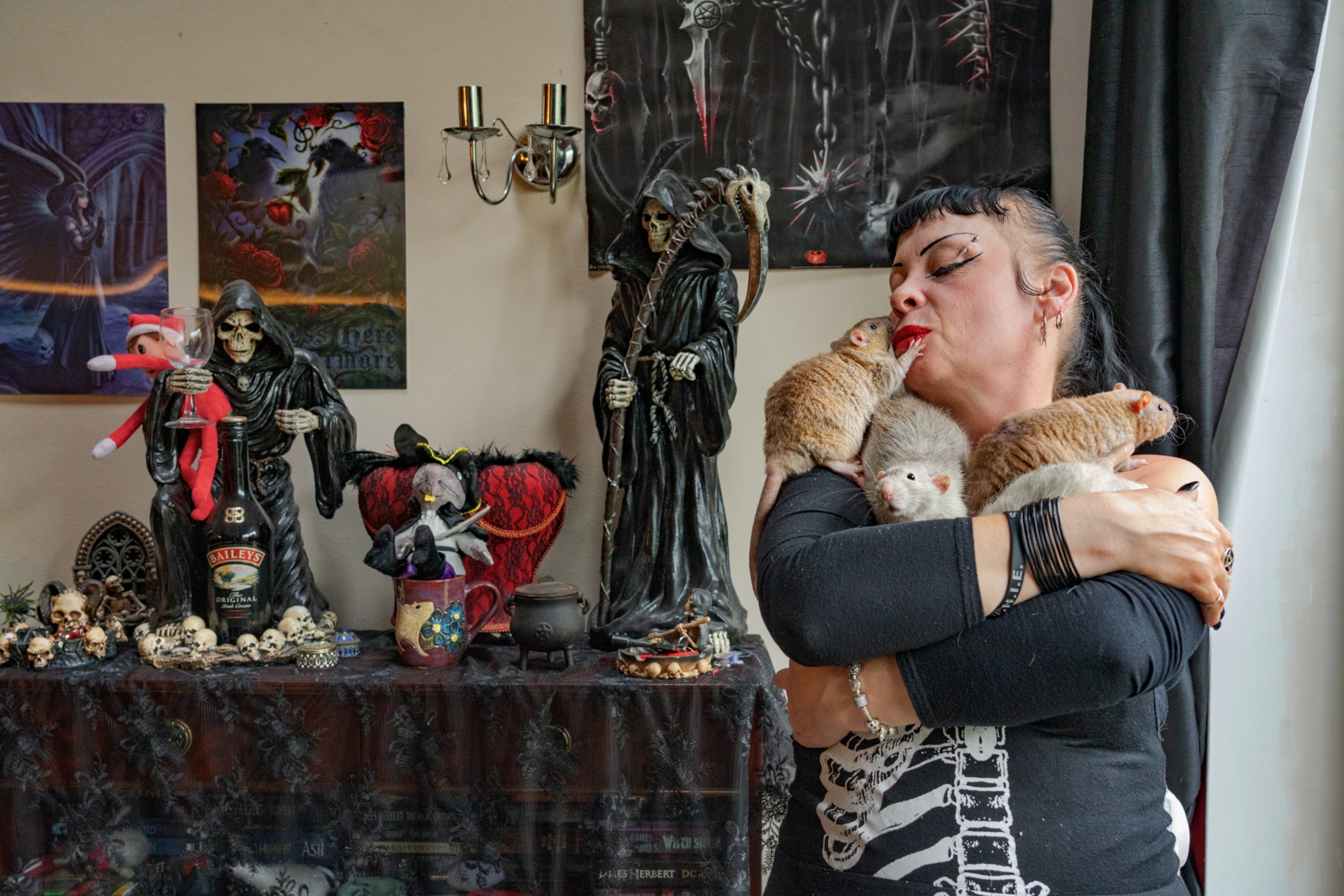 a women in black holding and kissing pet rats in front of halloween like decorations