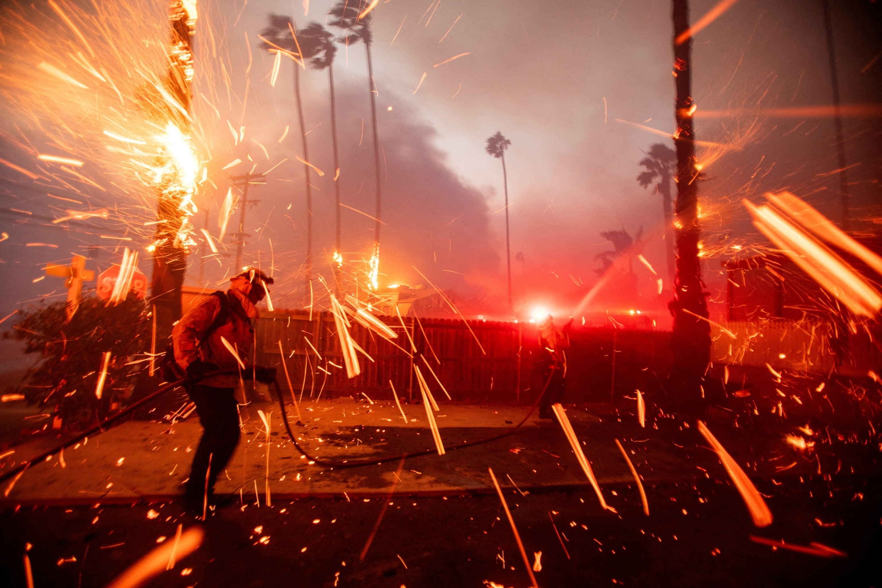 Fire embers fly around firefighters.