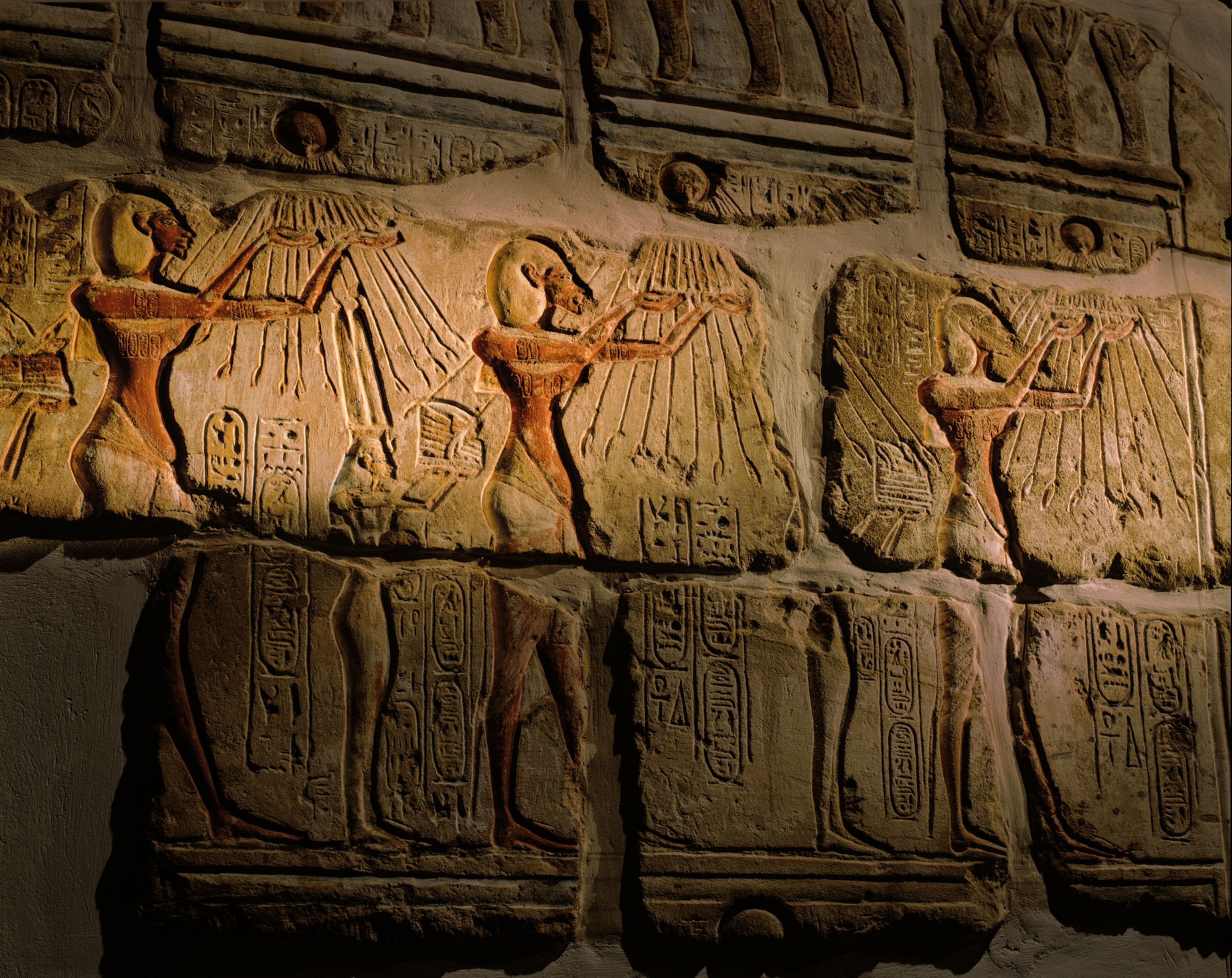 Figures carved into a wall raising their hands towards sun rays