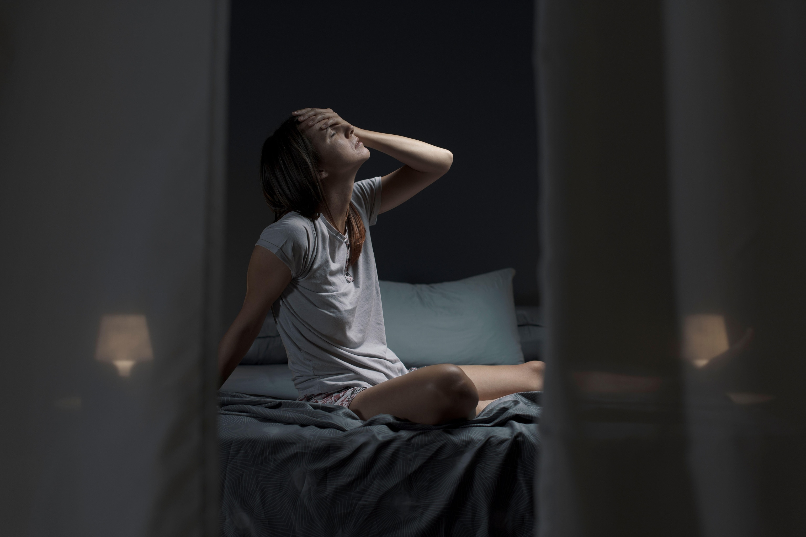Tired woman sitting in bed at night with open window, she is unable to sleep due to being hot