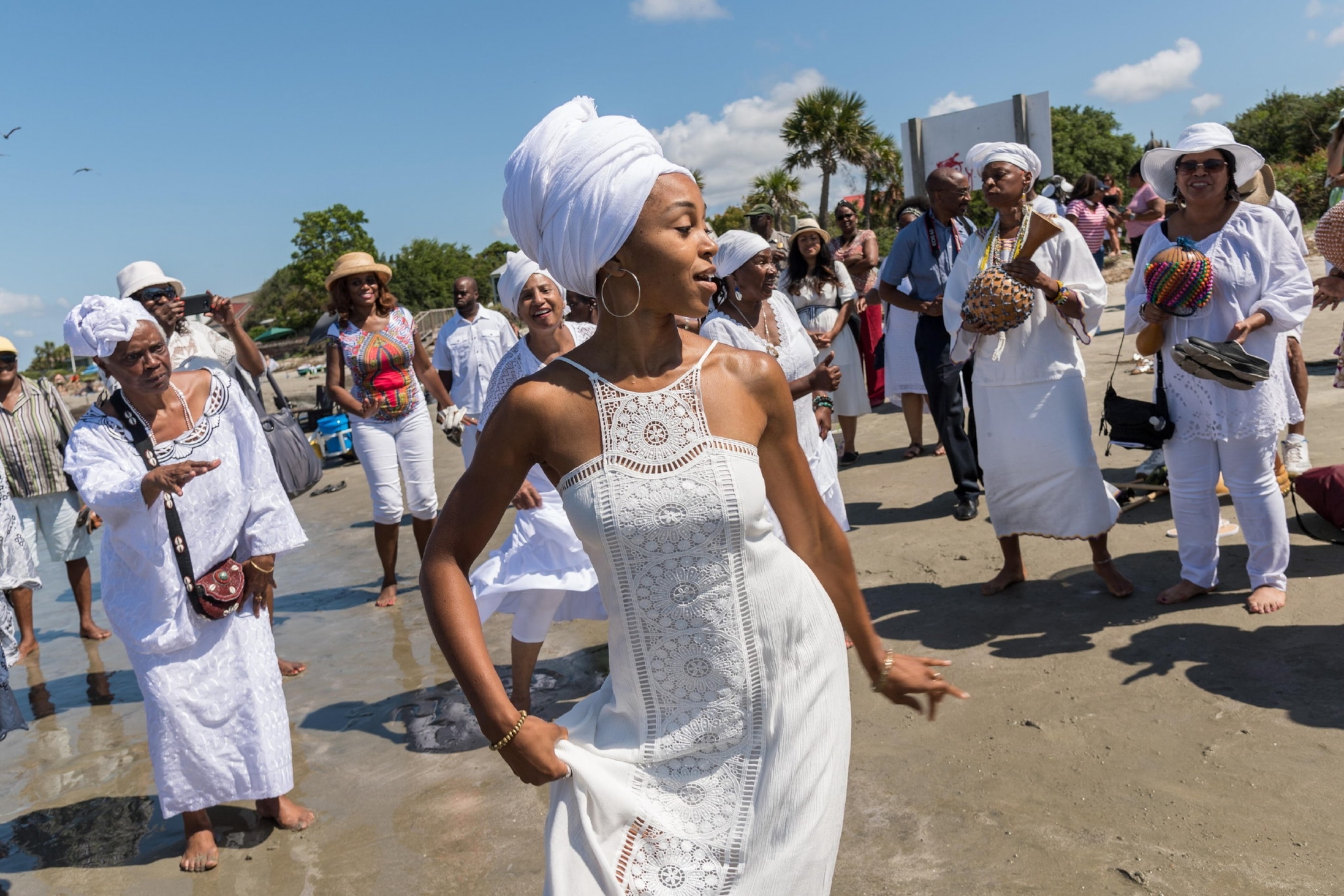 People wearing white dancing along a shore