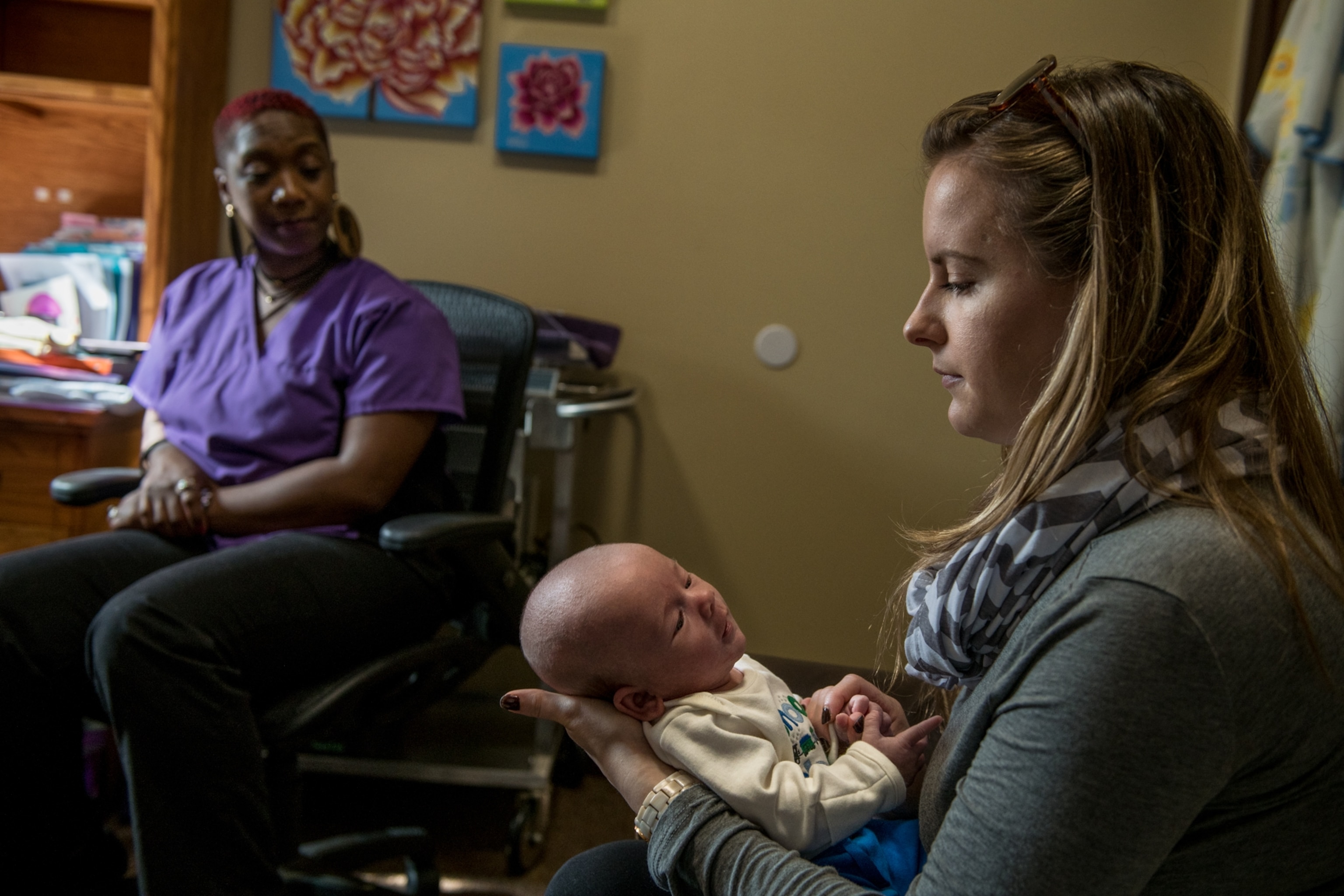 a tow women sitting on a couch and talking, one is holding a newborn baby