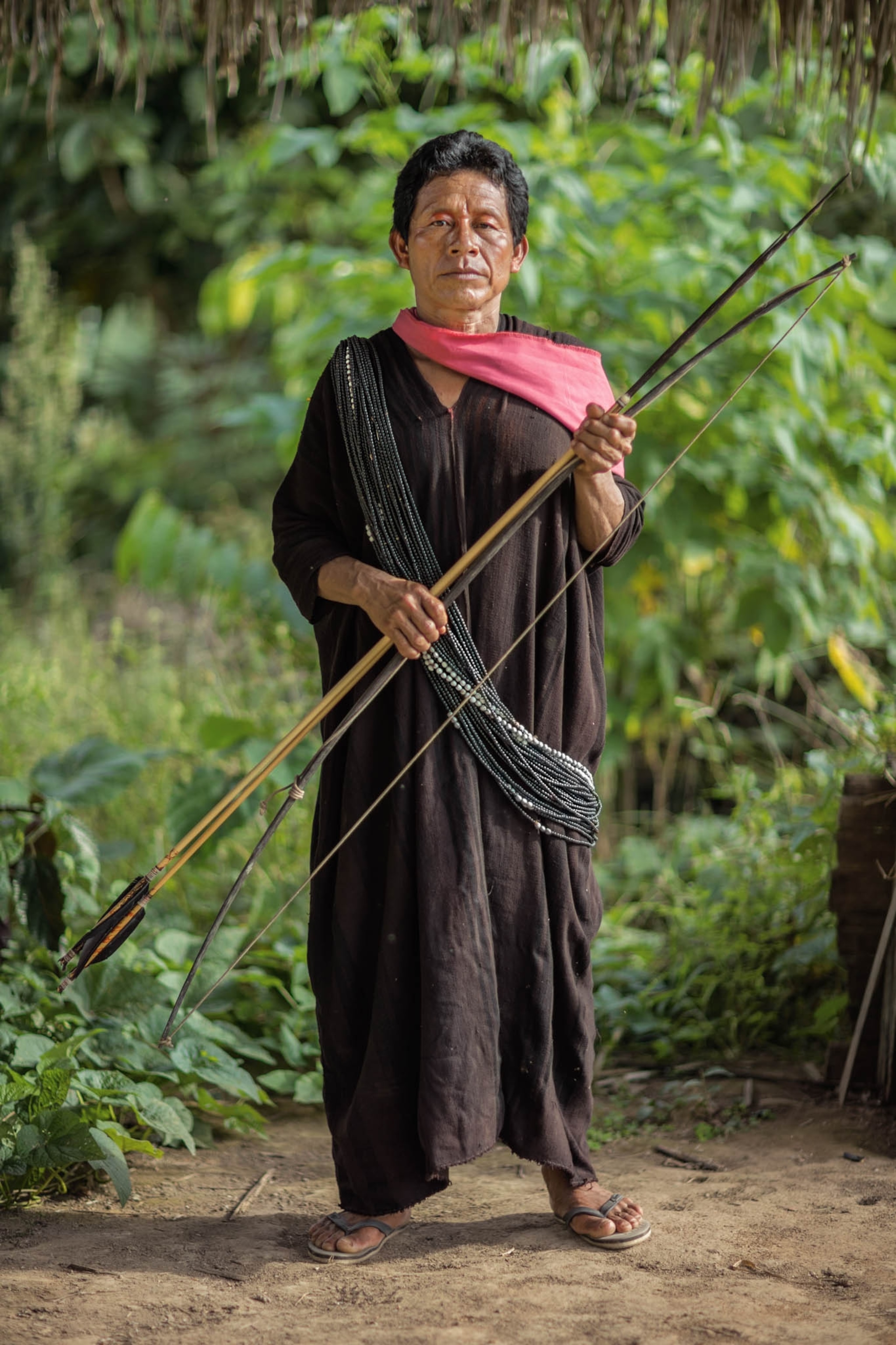 a man in a brown smock with a pink scarf holding a bow and arrows