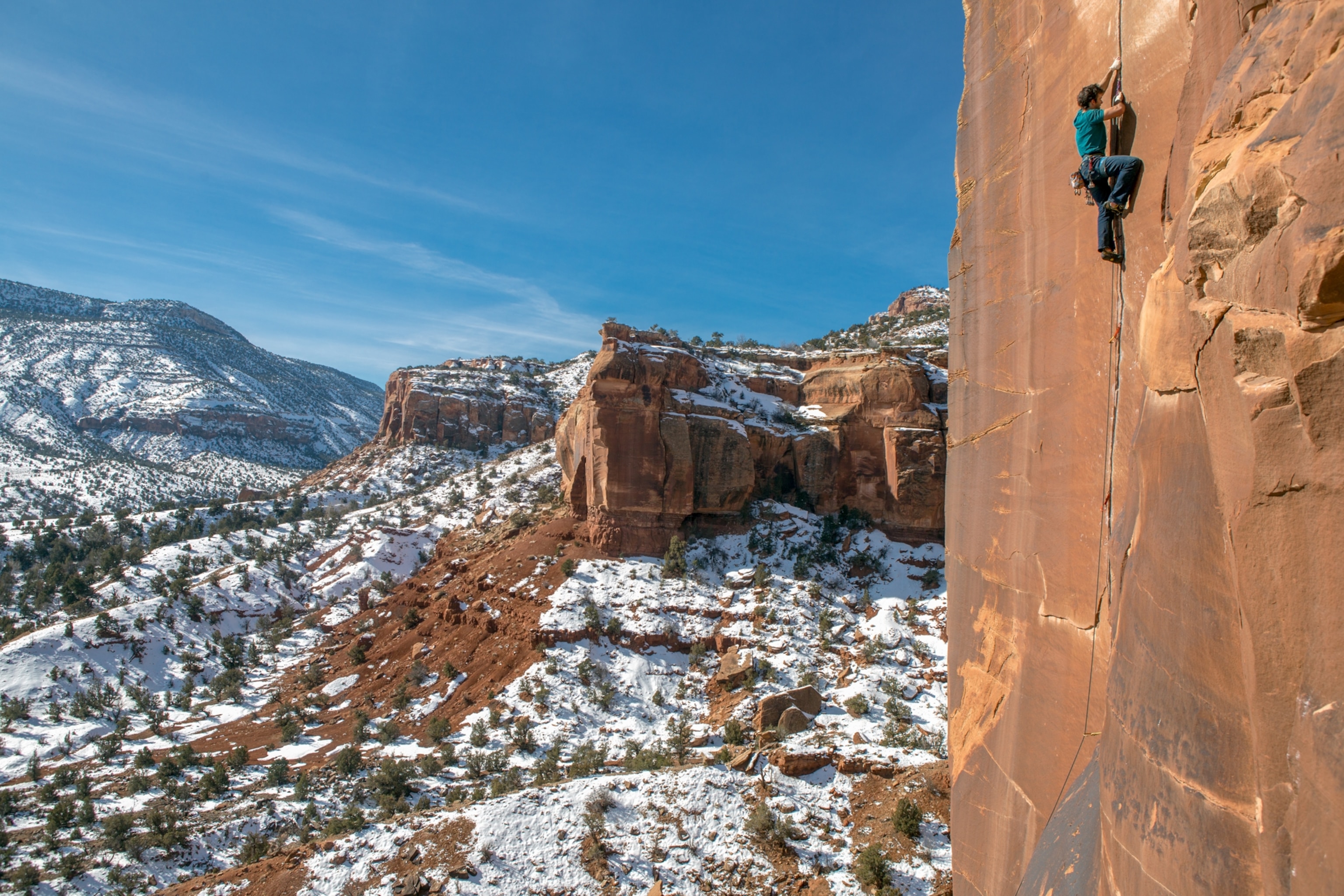 A man climbs a cliff you can see the beauty of Colorado in the landscape behind him.