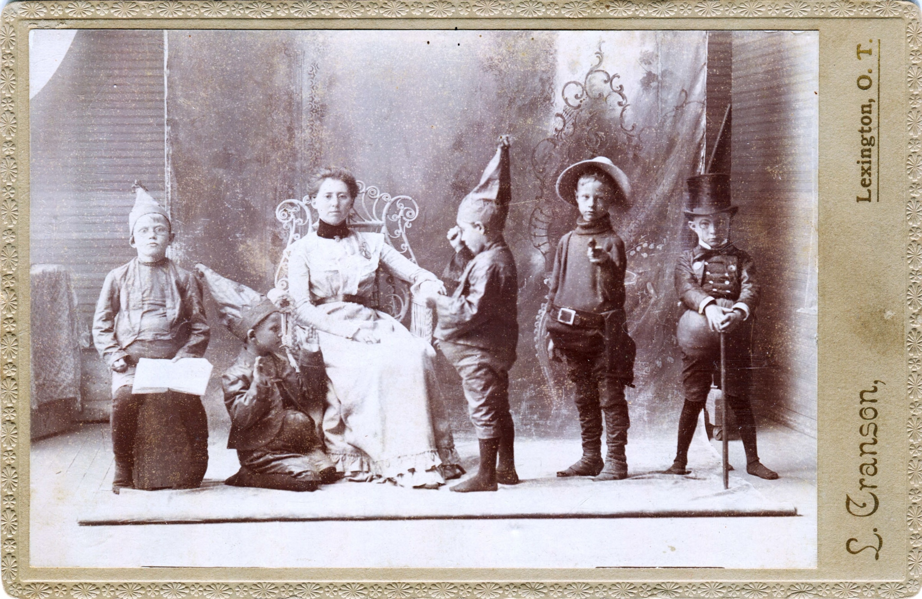 a young woman and five boys in Halloween costumes around 1890