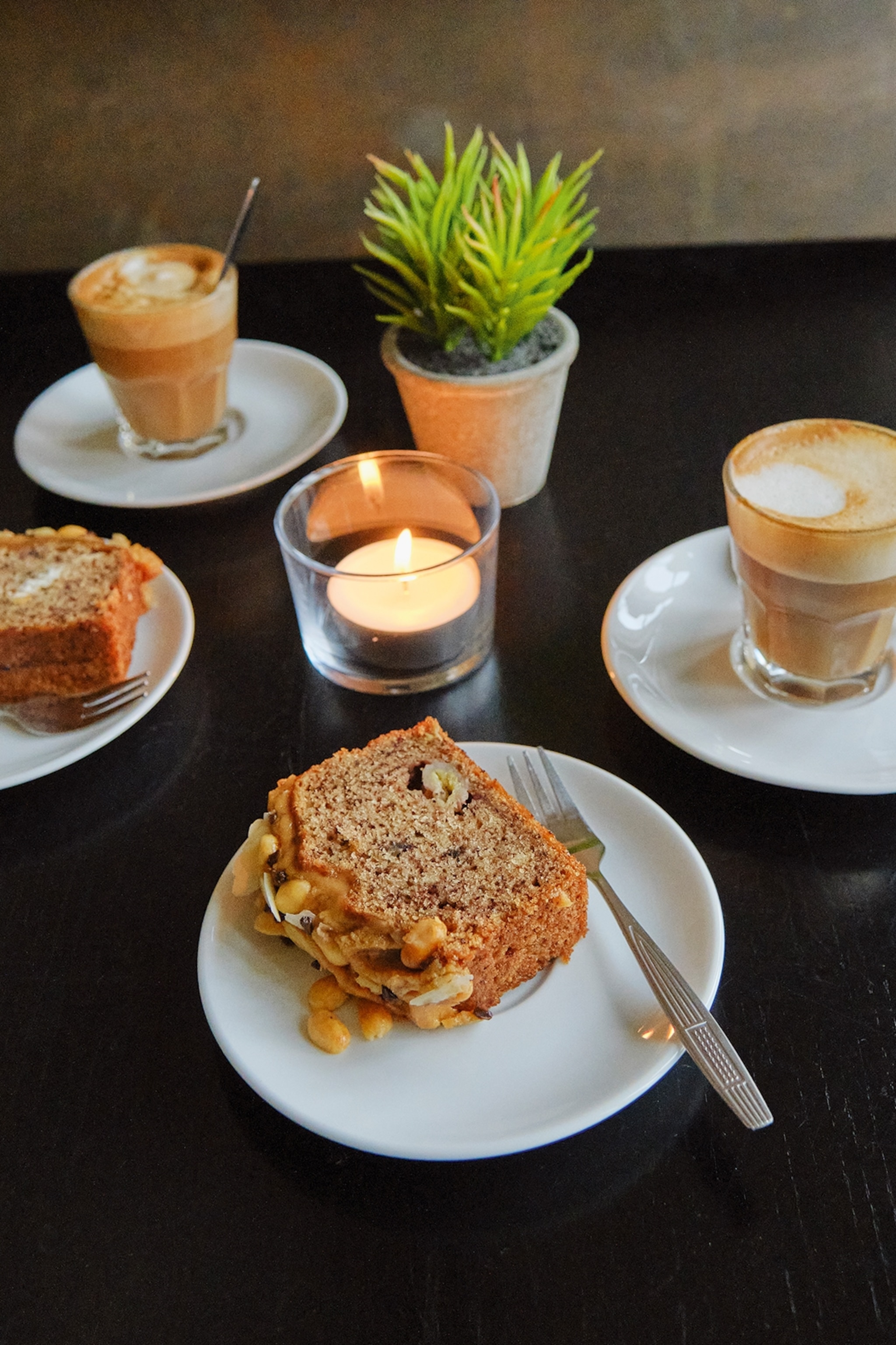 A close up of dishes and coffees on a black table.
