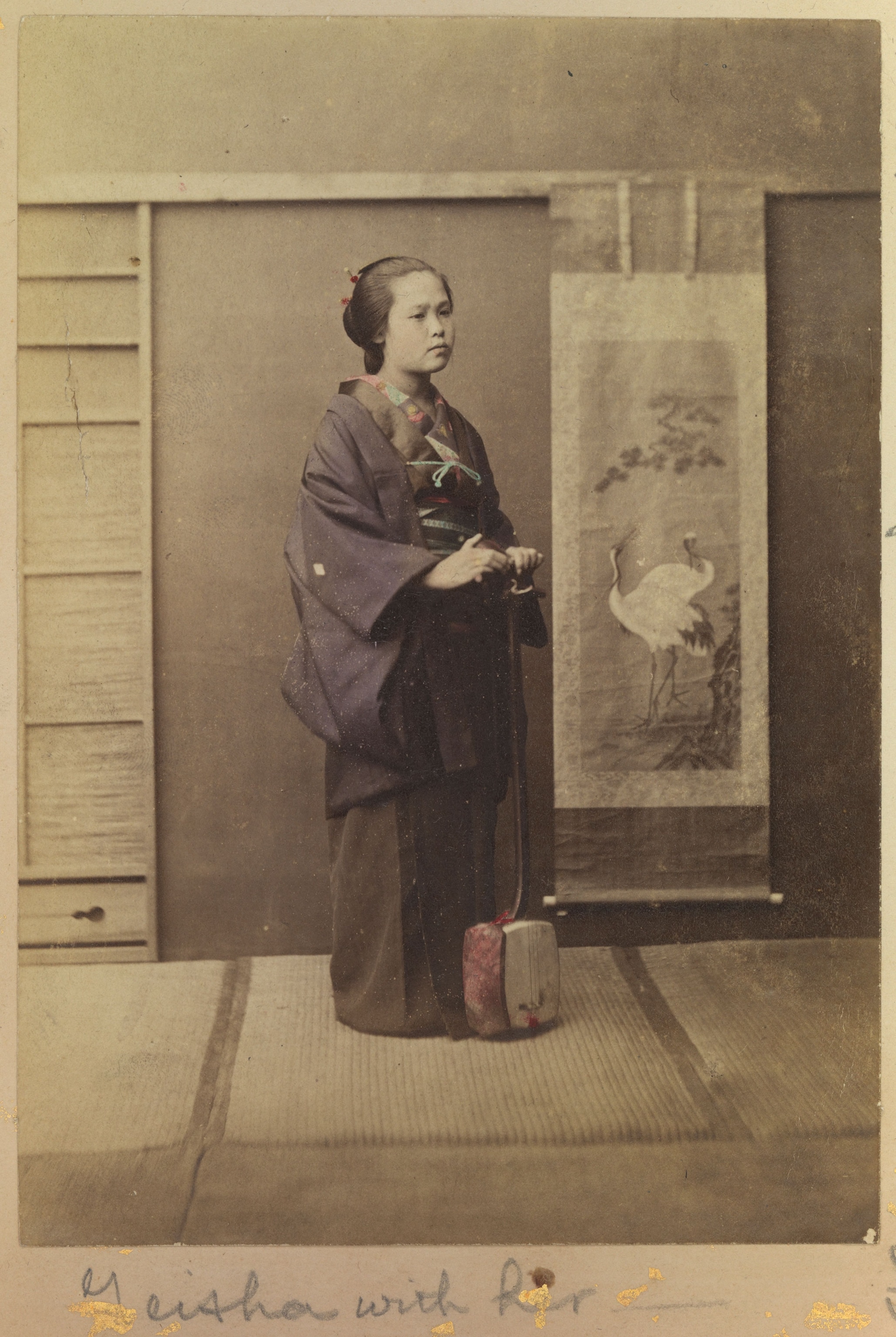 A geisha stands holding her musical instrument, a samisen in Japan