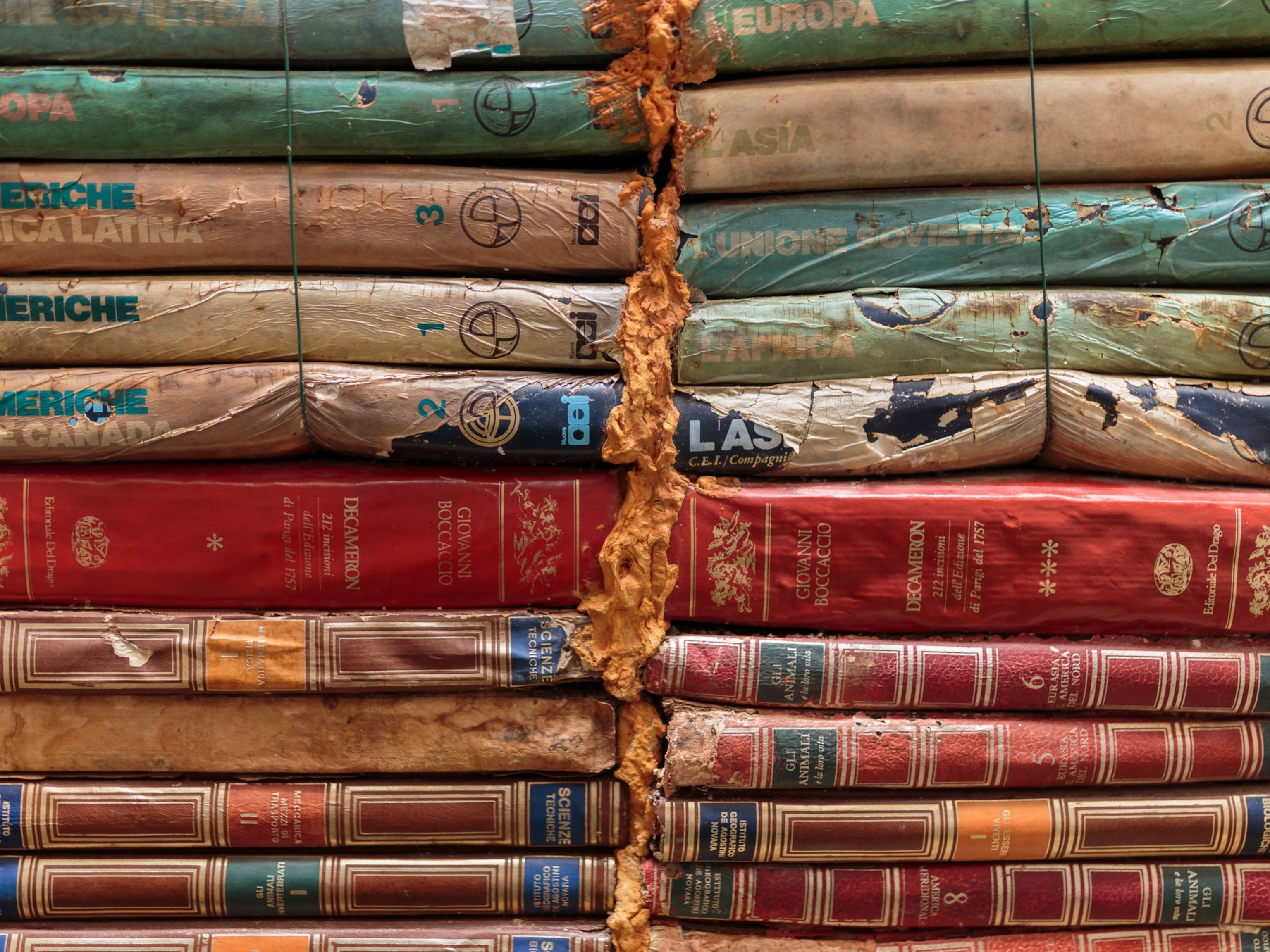The spines of stacked books, which are crinkled and partially stained as a result of water damage