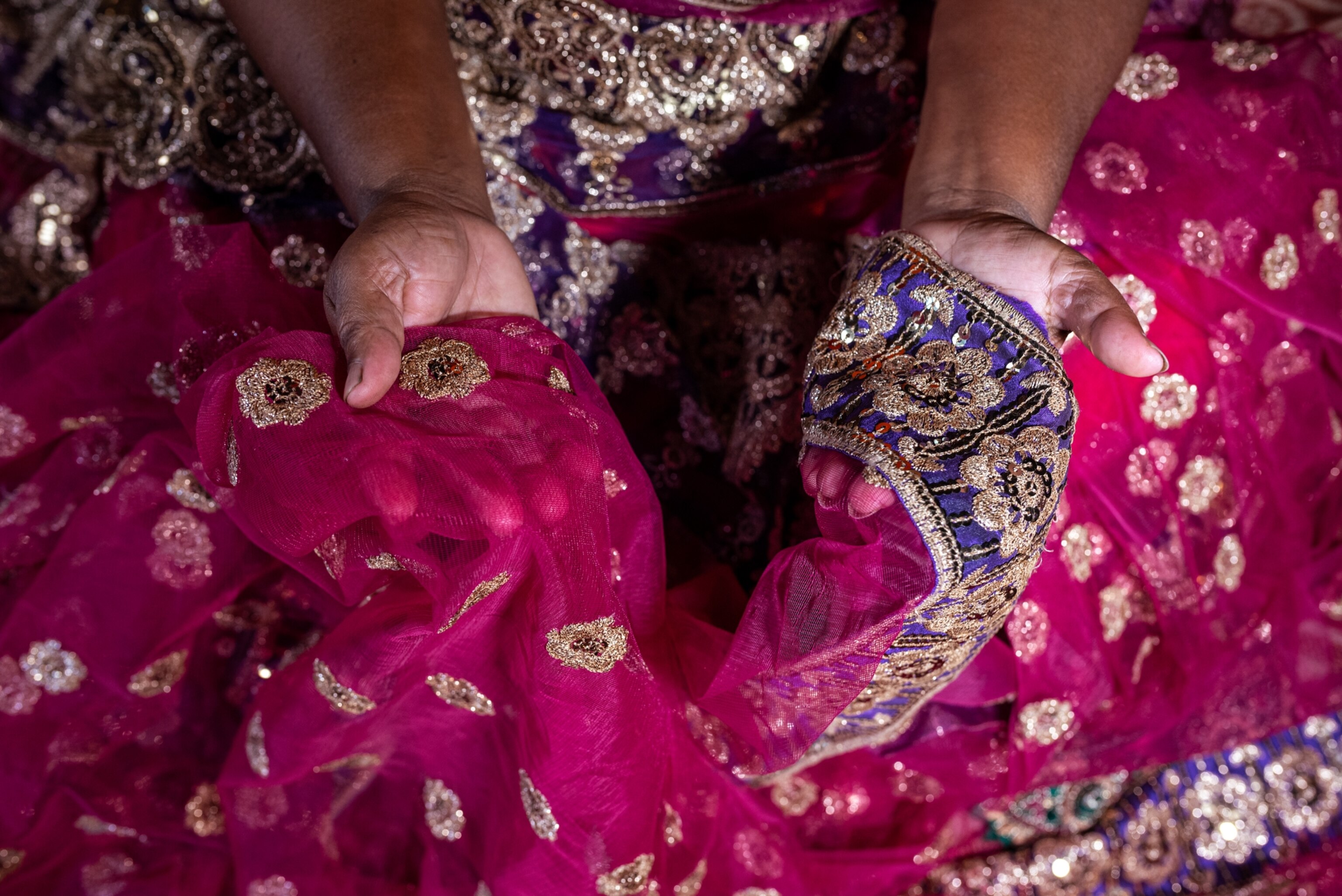 hands holding up a pink sari with light gold detailing