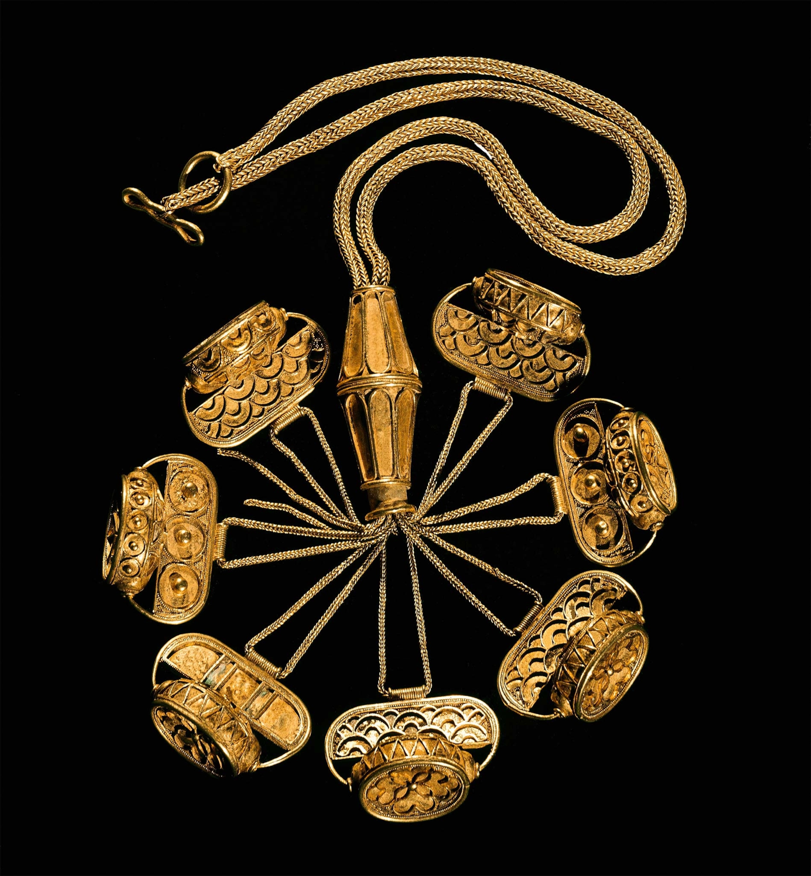 A gold necklace features seven seals of Egyptian scarabs on a black background