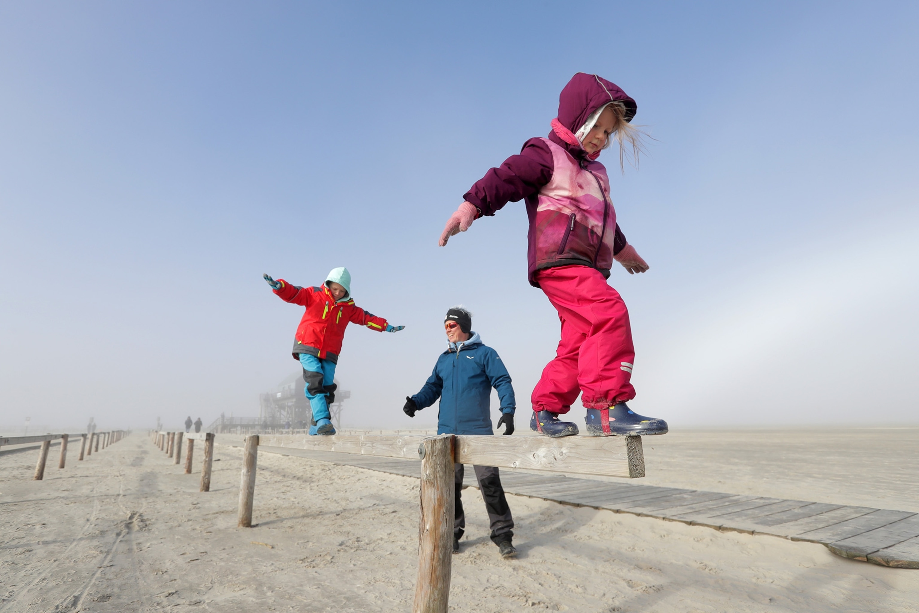 Fog on the beach. Children balance on a beam.