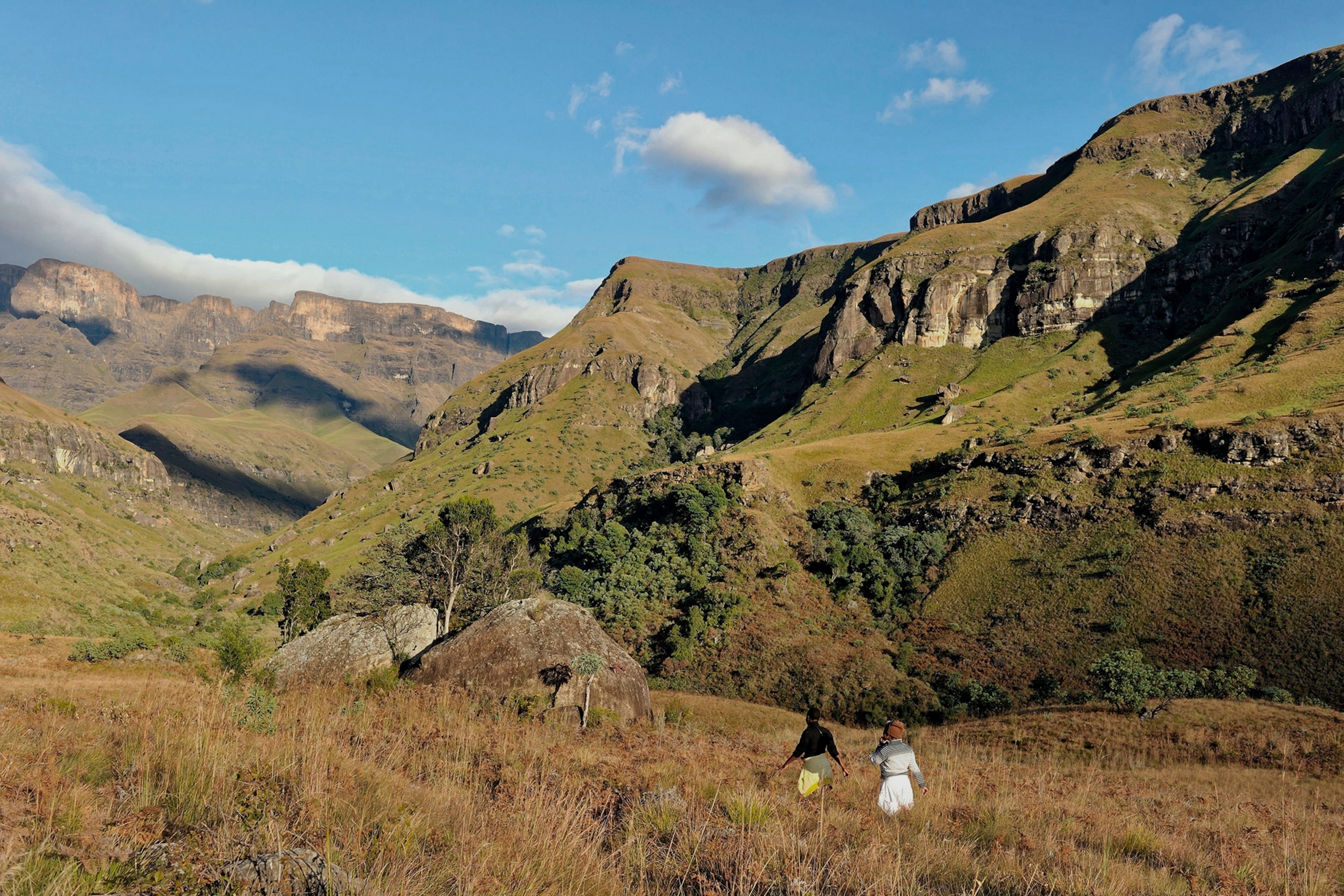Two people walking through grassland in a national park surrounded by mountains