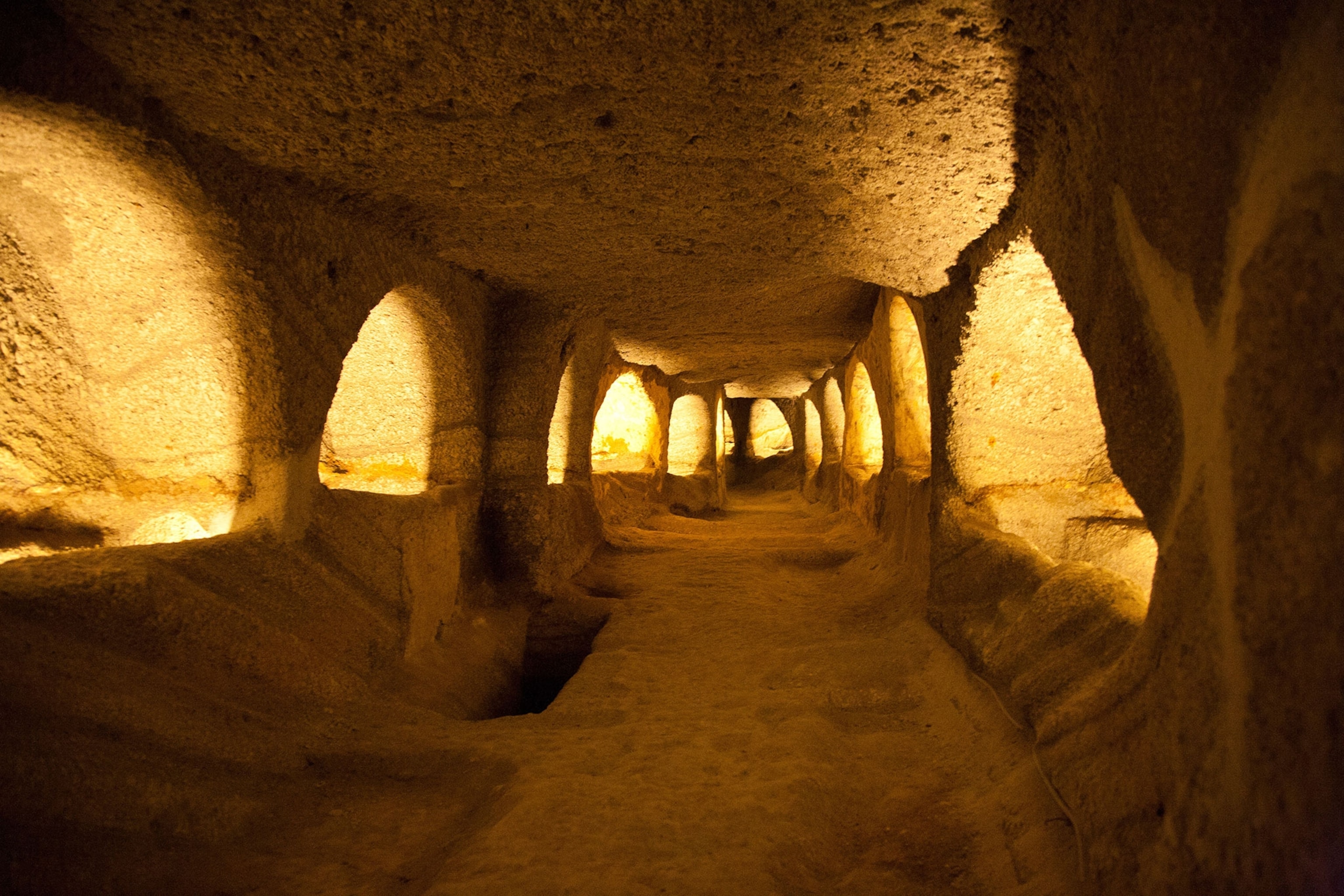 Underground catacombs tunnel with light projecting from arches carved into the side walls.